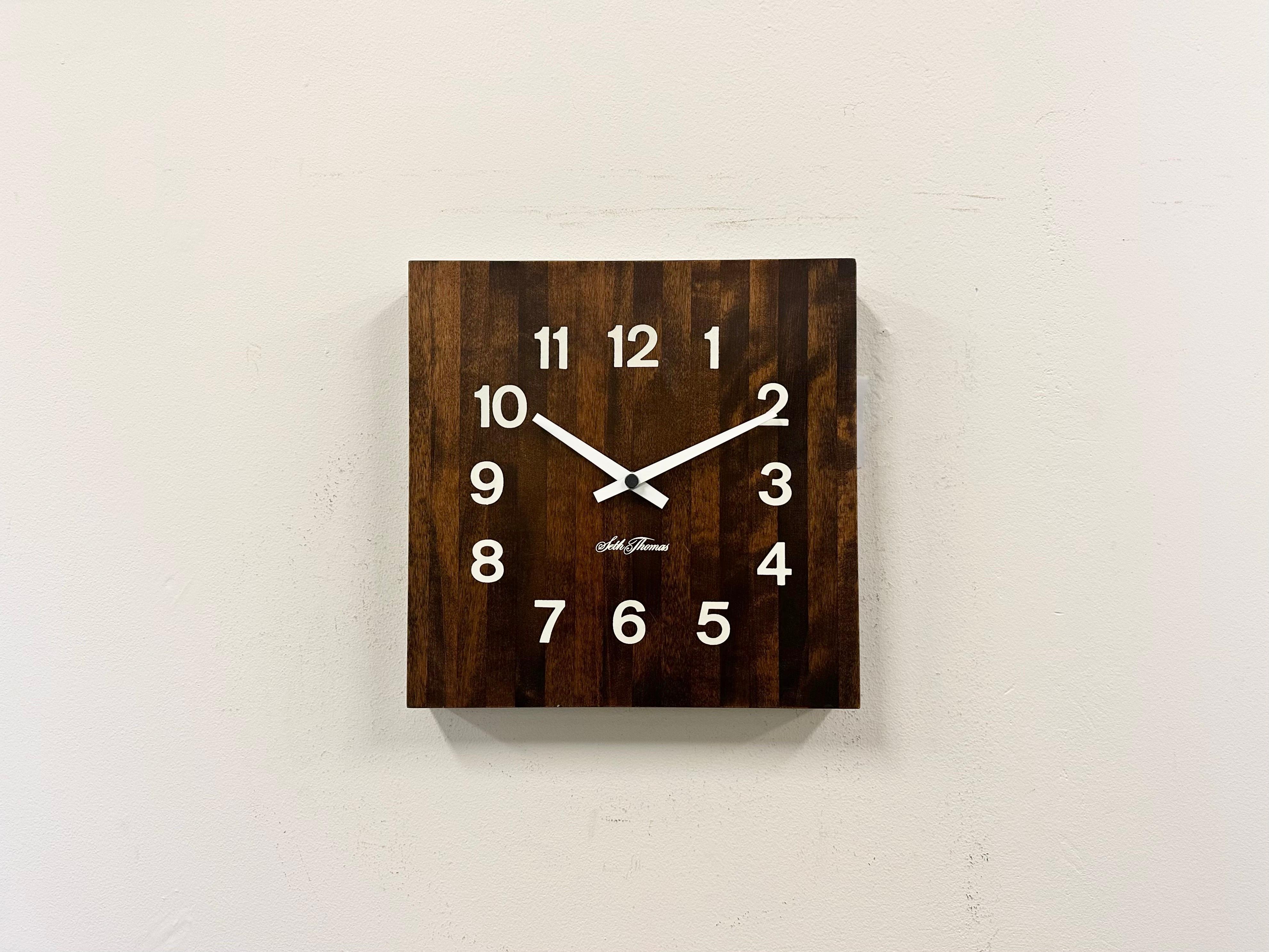 Wanduhr, hergestellt von der Seth Thomas Clock Company in den USA in den 1980er Jahren. Sie hat ein braunes, holzfurniertes Zifferblatt und Aluminiumzeiger. Das Stück wurde in ein batteriebetriebenes Uhrwerk umgewandelt und benötigt nur eine