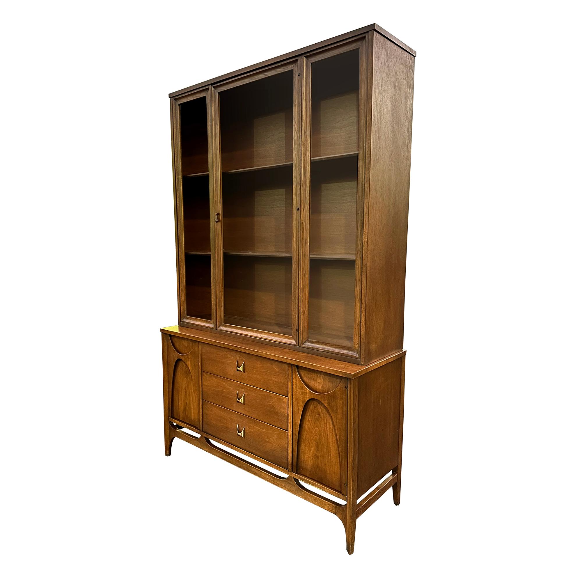 1960s Mid-Century Modern Brasilia walnut credenza with glass hutch top by Broyhill. The bottom piece features 3 center drawers with original brass tone hardware and 2 cabinets. The top piece features a glass door and 2 shelves inside. Good vintage