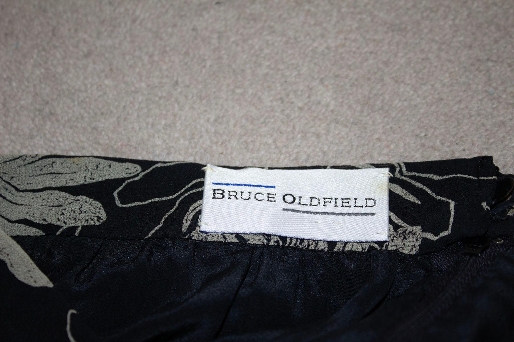 Un superbe tailleur pantalon en soie vintage de Bruce Oldfield. 
Ce costume en soie fait sur mesure présente un joli imprimé, avec un pantalon et un haut doublés.  Le haut est doté d'une ouverture zippée sur le côté et d'un bouton dans le dos. Ils