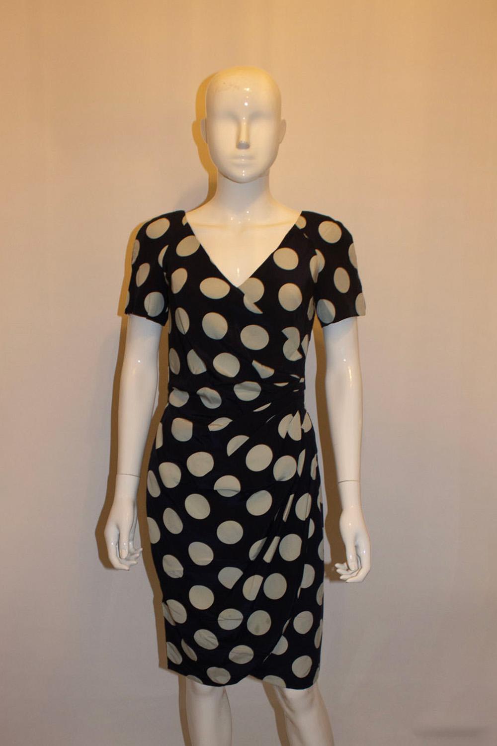 A fun vintage dress by British designer , Bruce Oldfield favorite of Queen Camilla. The dress is in super soft silk, with a blue background and ice blue colour spots.  The dress has a wrap over front and tulip skirt, with short sleaves and a central