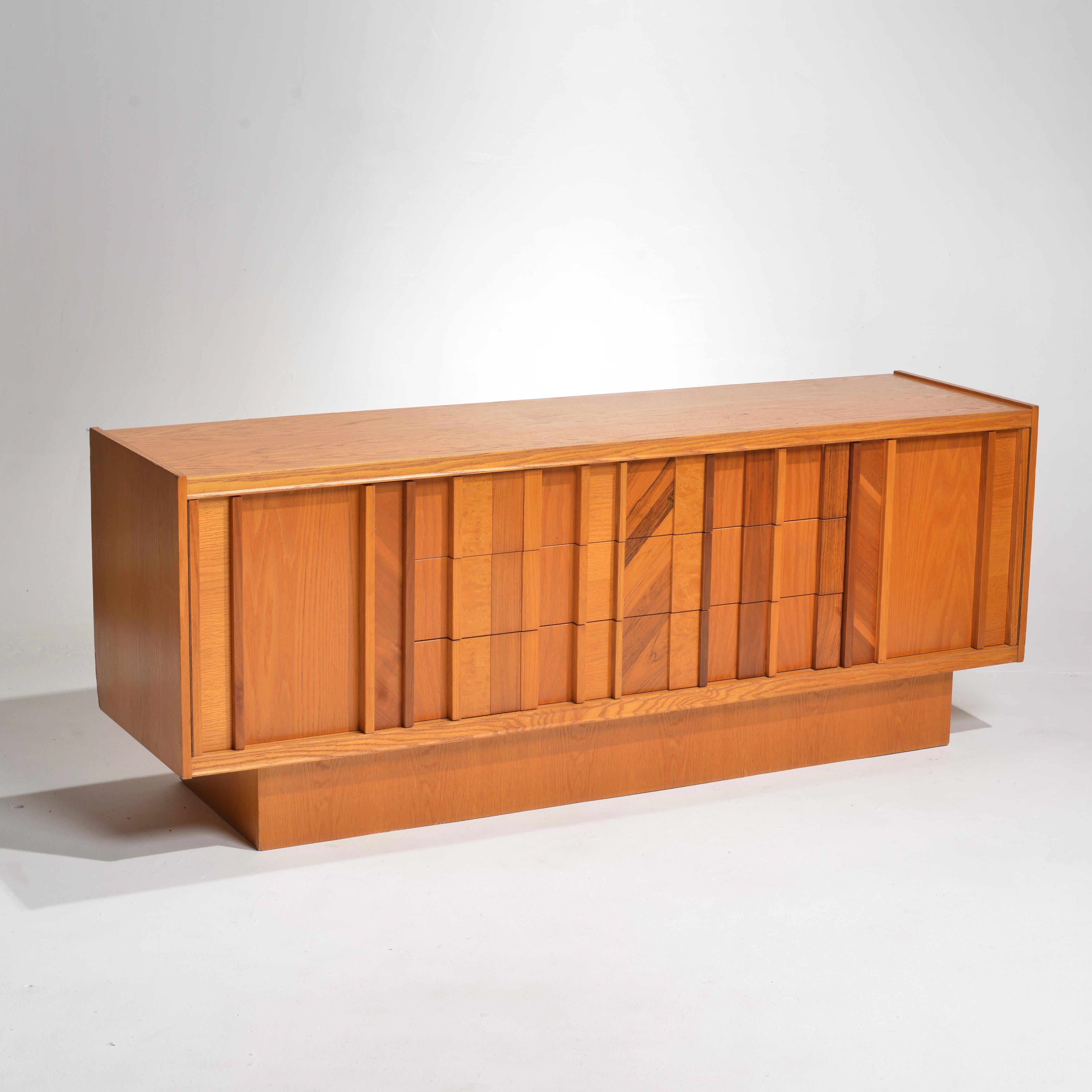 This stunning Vintage Brutalist Credenza Dresser features a bold yet classic combination of Maple Burl, Walnut, Rosewood, and Oak. The design is decorated with striking geometric patterns and sculptural elements that give it a bold and unique look.