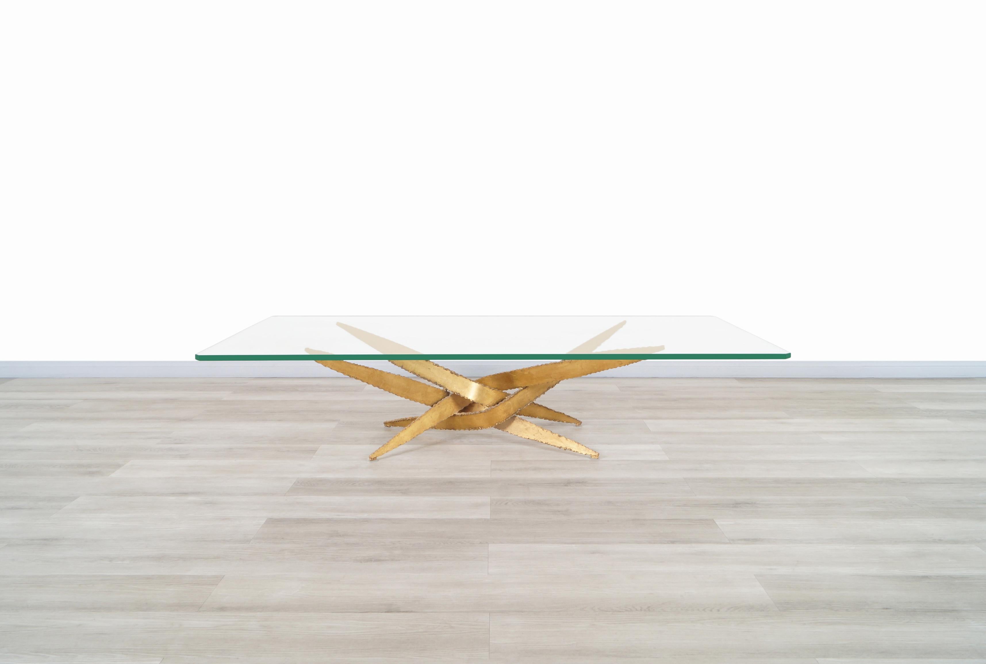 Vintage Brutalist coffee table designed by Silas Seandel in the United States, circa 1970s. This wonderful coffee table has an unusual design on the base. It's formed with four separate steel pieces in a gold finish sculpturally arranged, expressing