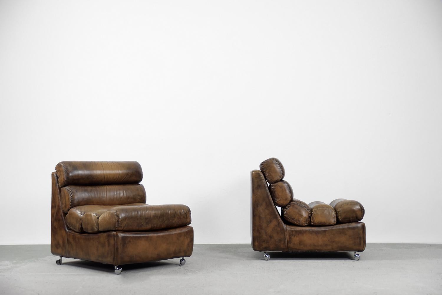 This rare brutalistic set of two armchairs was manufactured in the 1960s. This set has been upholstered with natural leather in shades of brown. The pillow is fastened with strong bur. The chair are characterized by semicircular and aerodynamic
