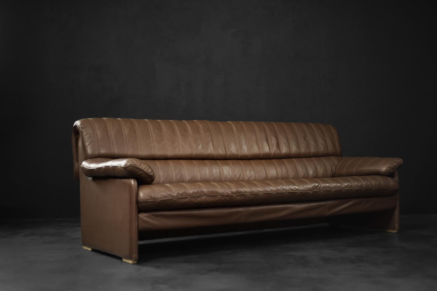 This long, four-seater sofa was manufactured in Germany during the 1970s in a brutalist style. The frame is made of solid wood. It is upholstered in high-quality, thick natural leather in amber brown with natural patina. The leather has visible