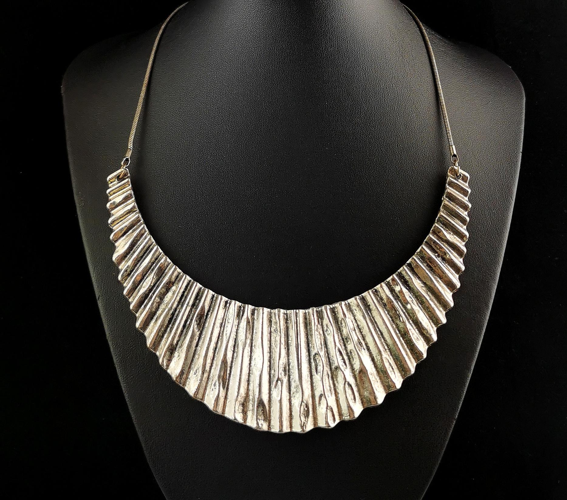 A striking vintage Brutalist style metal bib necklace.

The crescent shaped bib is made from rustic pleated steel with a weathered look and is adjoined with a base metal snake chain.

It is definitely a statement piece and really stands