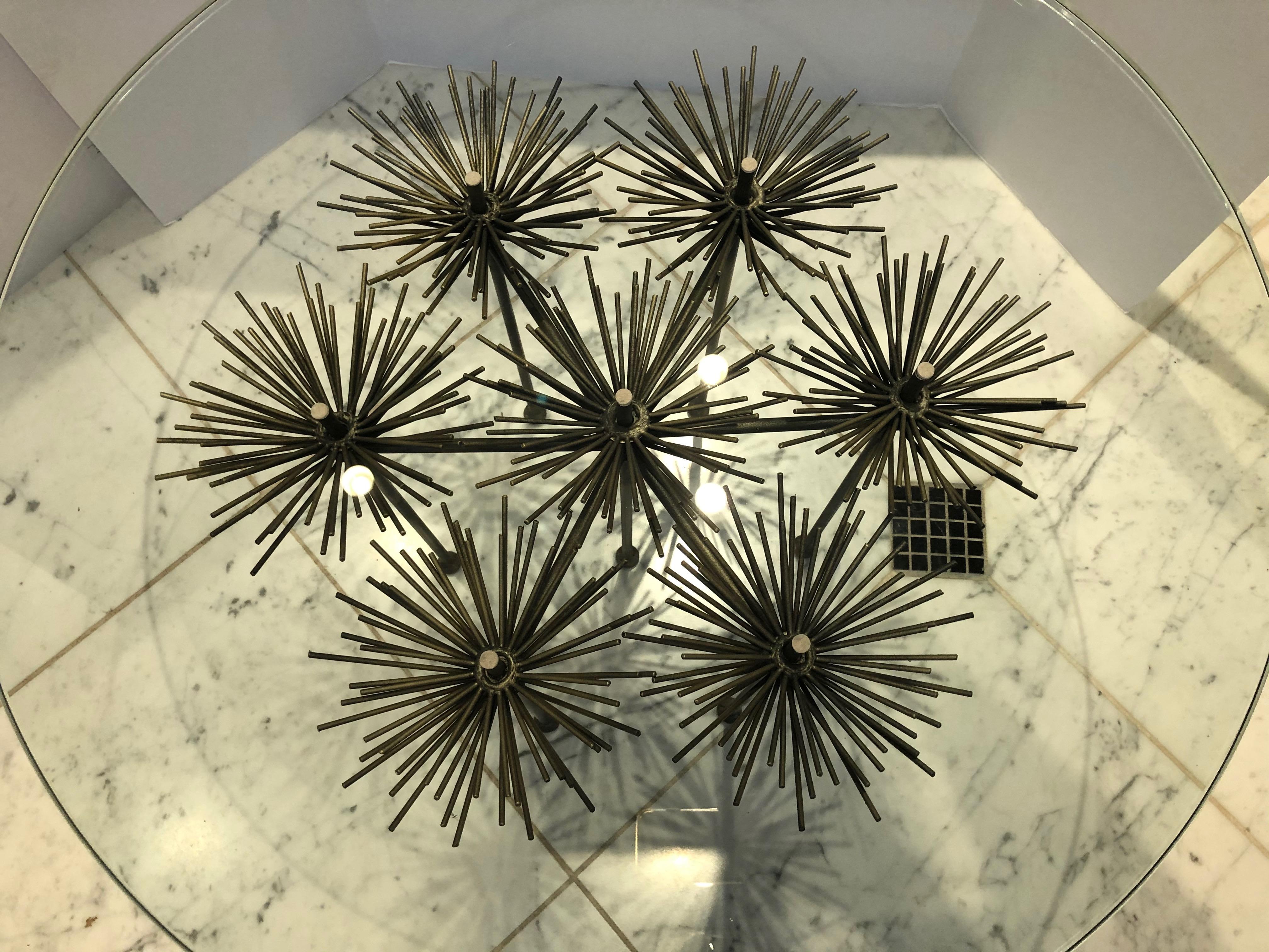 A sophisticated side table in the Brutalist style comprised of a polished steel base and thick glass top (not attached). The base has ball feet with rods that extend upwards and burst into flower-like blooms. The round glass top is substantial at