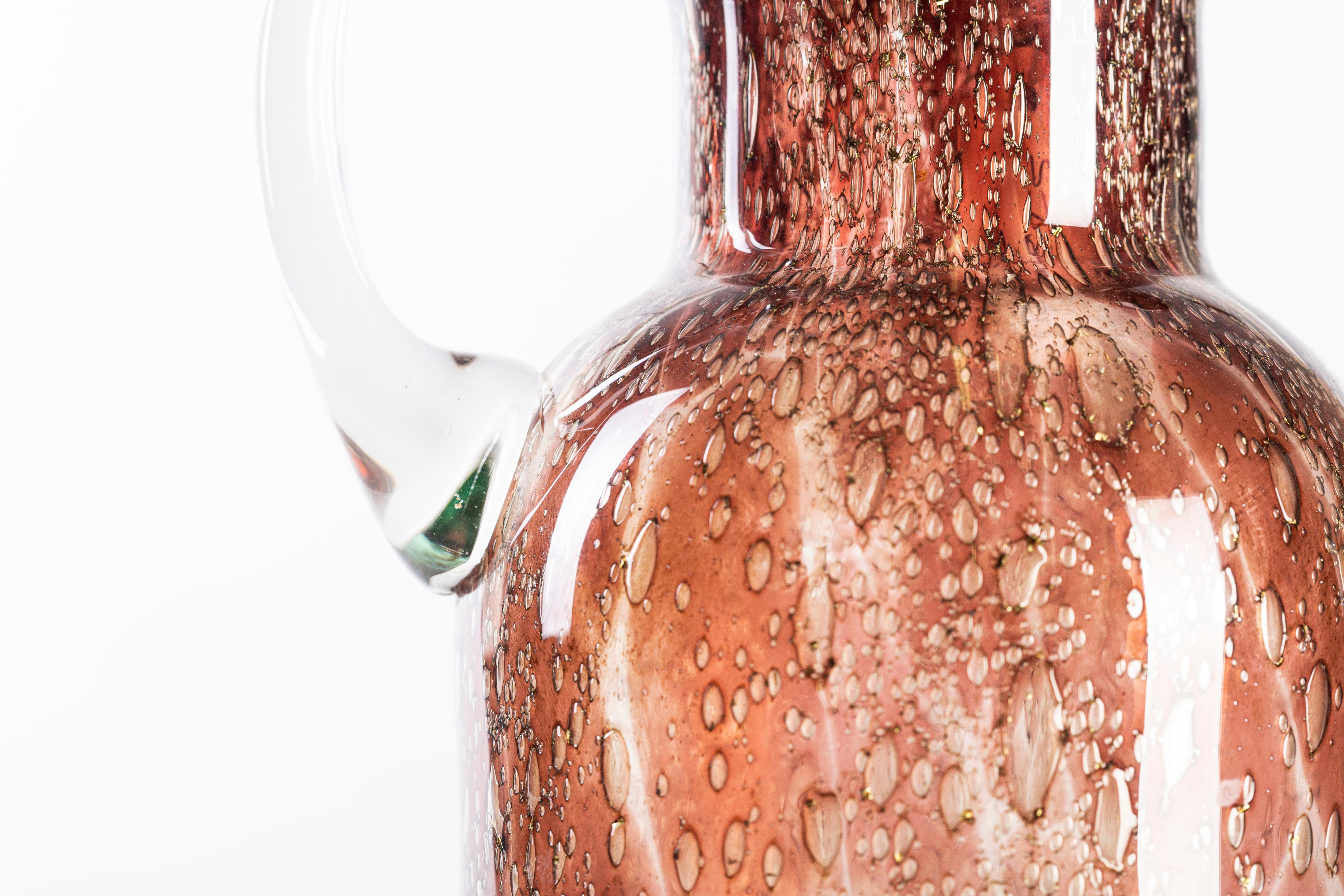 Bubble glass pitcher is a beautiful original bronze-colored glass decorative object:

Made in Italy vase realized in the 1970s of 20th century. 

Our specimen is a wonderful glass pitcher with a cylindric body and a transparent handle.

The
