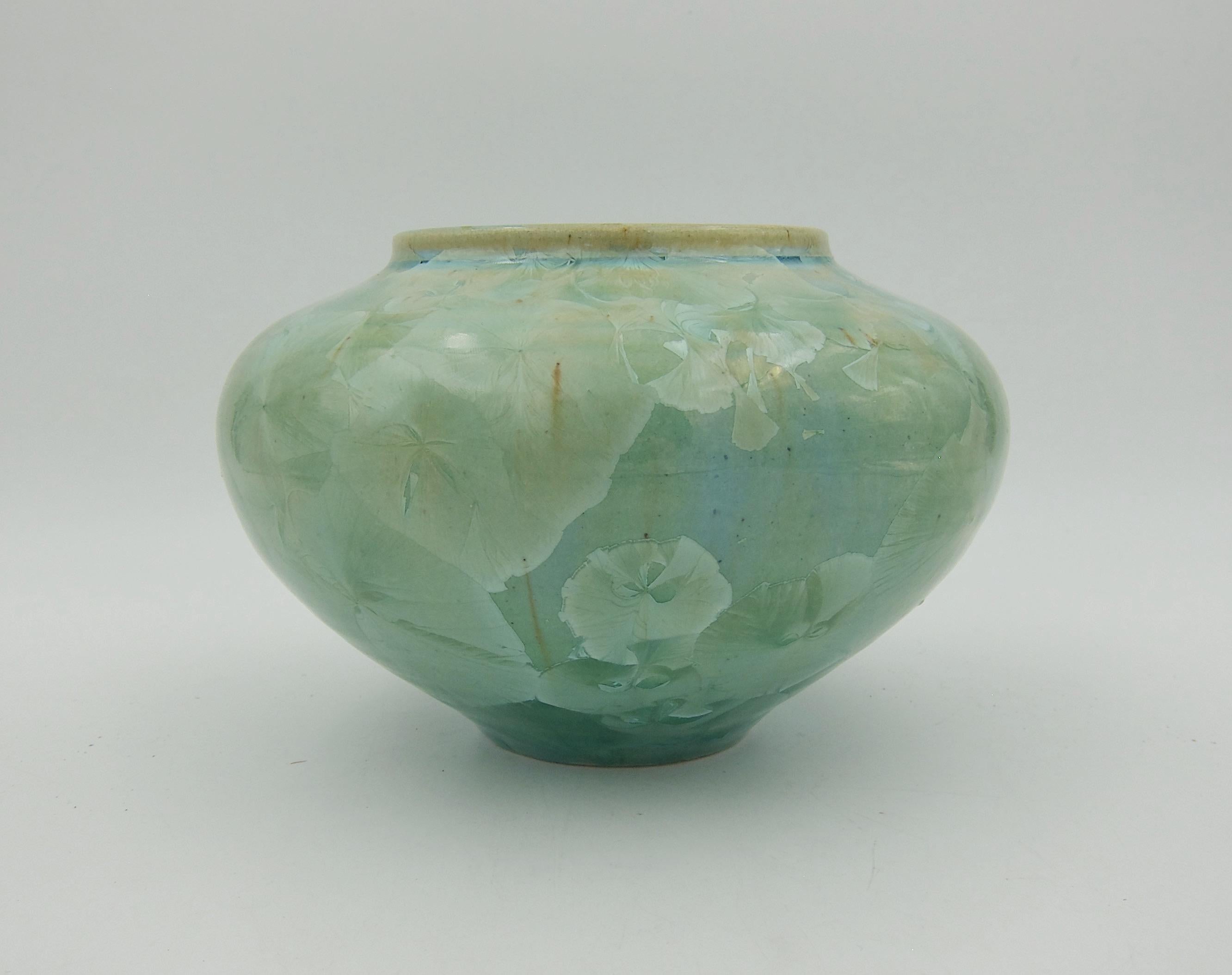 A hand-thrown and signed vintage studio pottery vase from 1994 with a sophisticated crystalline glaze in shades of glossy celadon green with large, overlapping icy crystalline clusters and accents of tan and brown. The American potter is Bill