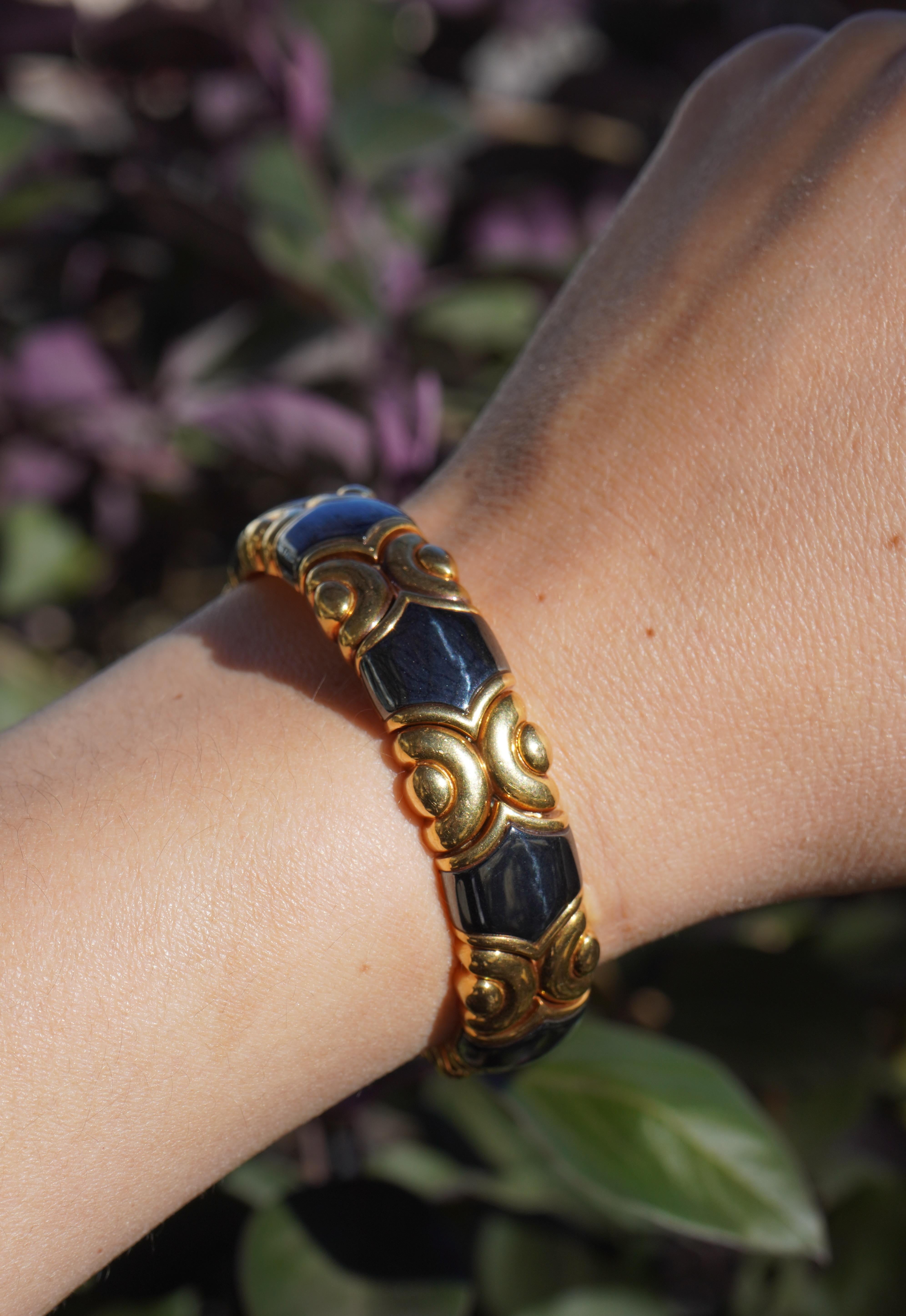 This Bvlgari 18K gold cuff bracelet features seven fancy-shaped hematite panels set within an ornate gold framework. The bracelet has an inner rose gold lining and weighs approximately 96 grams. It has an inner circumference of 6 1/4 inches and a