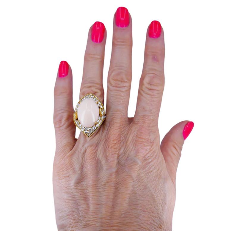 A luxurious vintage Bulgari Angel Skin coral diamond ring. The coral of a subtle, very soft pink hue is four-prong staged in a whimsical setting. The latter is designed as an oval gold frame with two sharp ends. The frame is adorned with diamonds