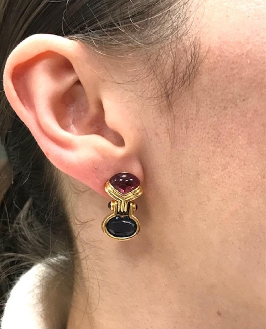 A pair of vintage Bulgari earrings, crafted in 18k gold, feature iolite, tourmaline, and rubies. 
The earrings consist of two elements: a cabochon-cut tourmaline at the top and a faceted iolite as the drop. These elements are connected by a hinge,