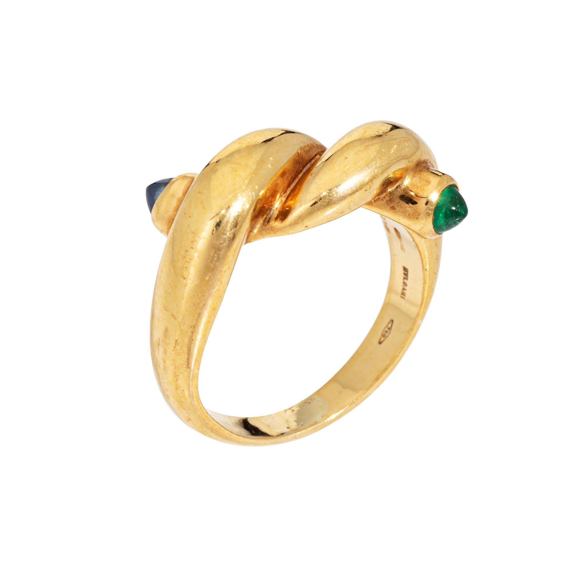 Vintage Bulgari knot ring set with a blue sapphire and emerald in 18k yellow gold.  

Pointed cabochon cut sapphire and emerald measure 3mm each. The sapphire is in good condition and free of cracks or chips. Minor chip to the emerald visible under