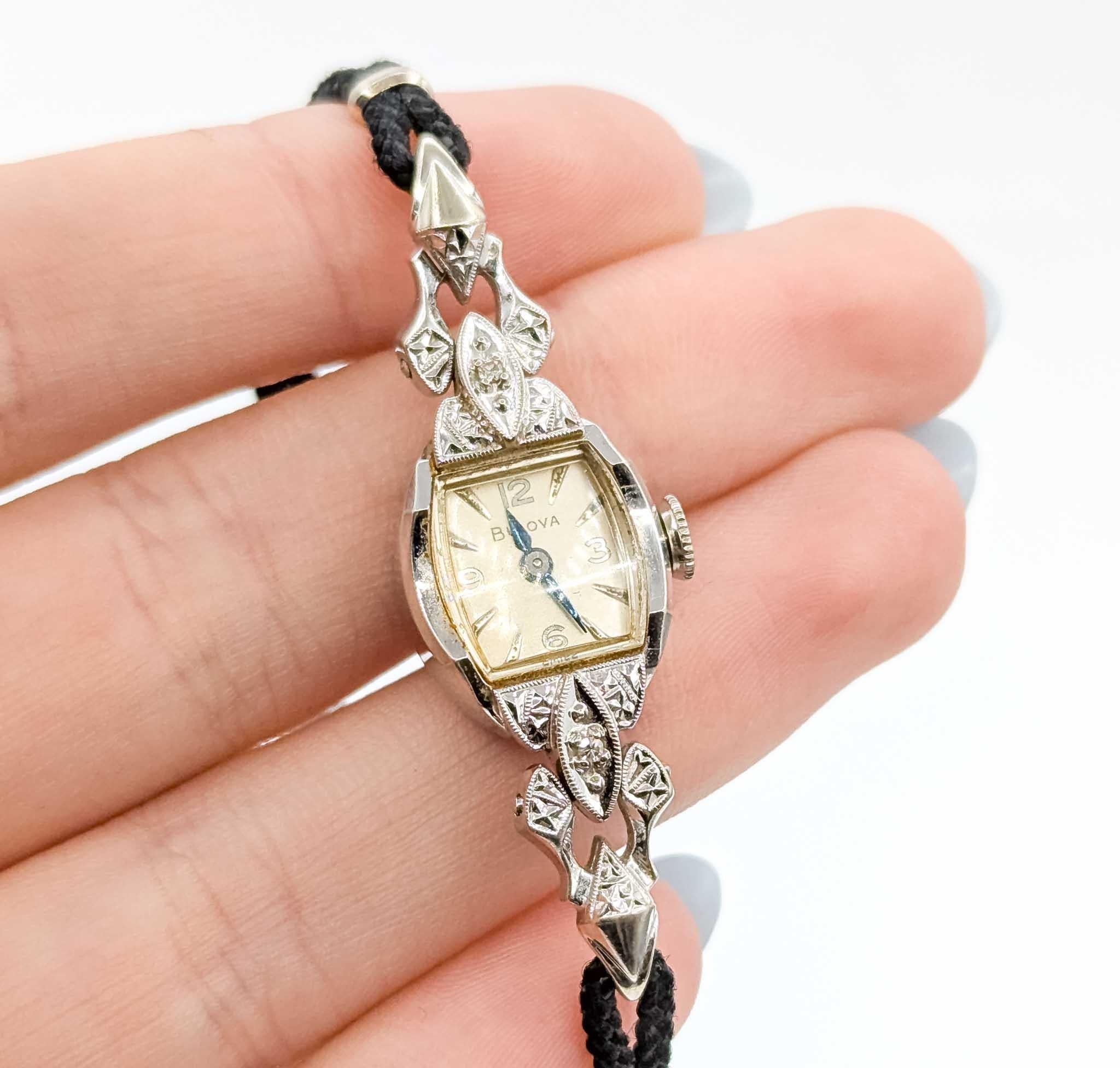 This elegant vintage Bulova wristwatch is crafted in 14k white gold and adorned with delicate single-cut diamond accents totaling approximately .03 carats. The watch features an elongated case with ornate filigree-style detailing at the shoulders,