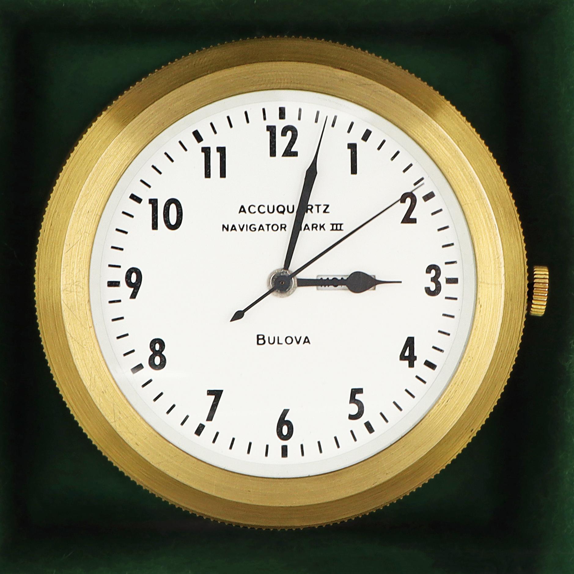 Este cronómetro marino Vintage Bulova Accutron Navigator Mark III es un reloj de precisión presentado en una elegante caja de madera con herrajes de latón. El cronómetro tiene una esfera blanca con números árabes negros, agujas negras de horas y