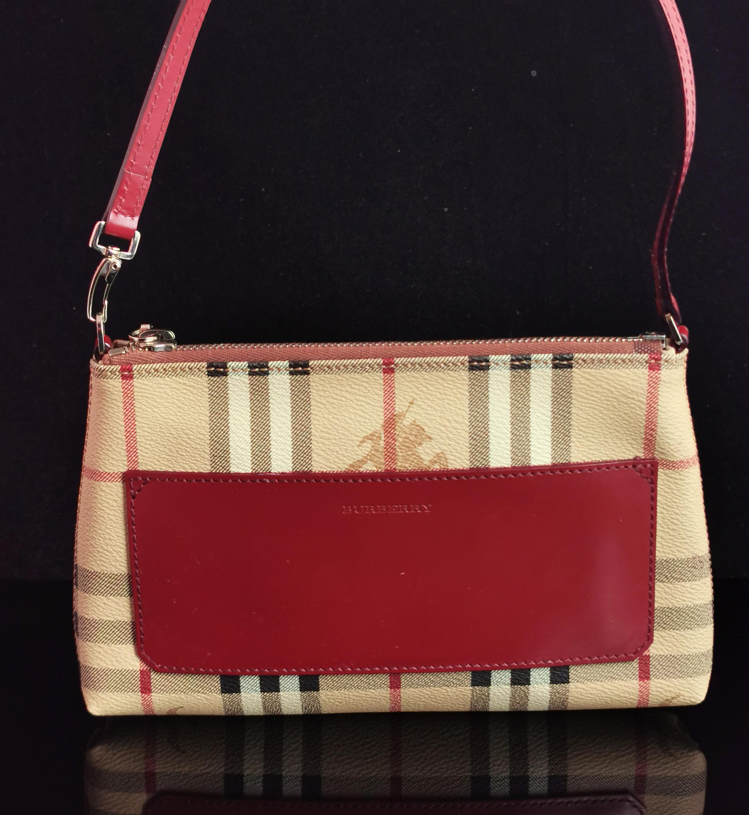 A stylish vintage Burberry pochette top handle or shoulder bag.

Classic Nova check in a coated and textured canvas with an oxblood red leather front, branded burberry.

It has a matching red leather handle and silver tone hardware including the