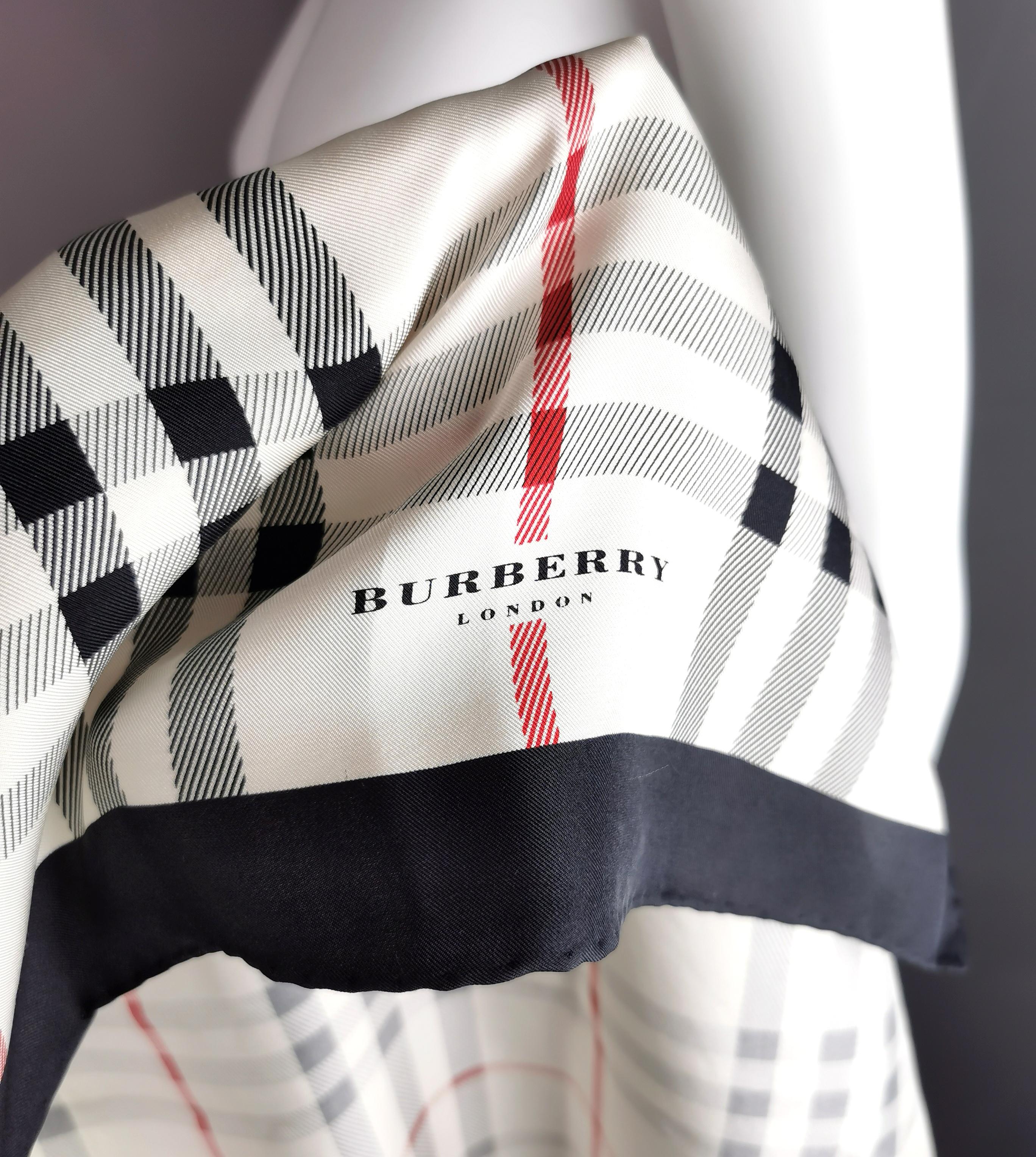Un élégant foulard vintage en soie à carreaux de Burberry.

Il s'agit d'une grande écharpe de forme carrée légèrement décalée, de couleur blanc cassé, rouge et noir, avec un imprimé à carreaux caractéristique.

Marquage imprimé au coin de l'écharpe