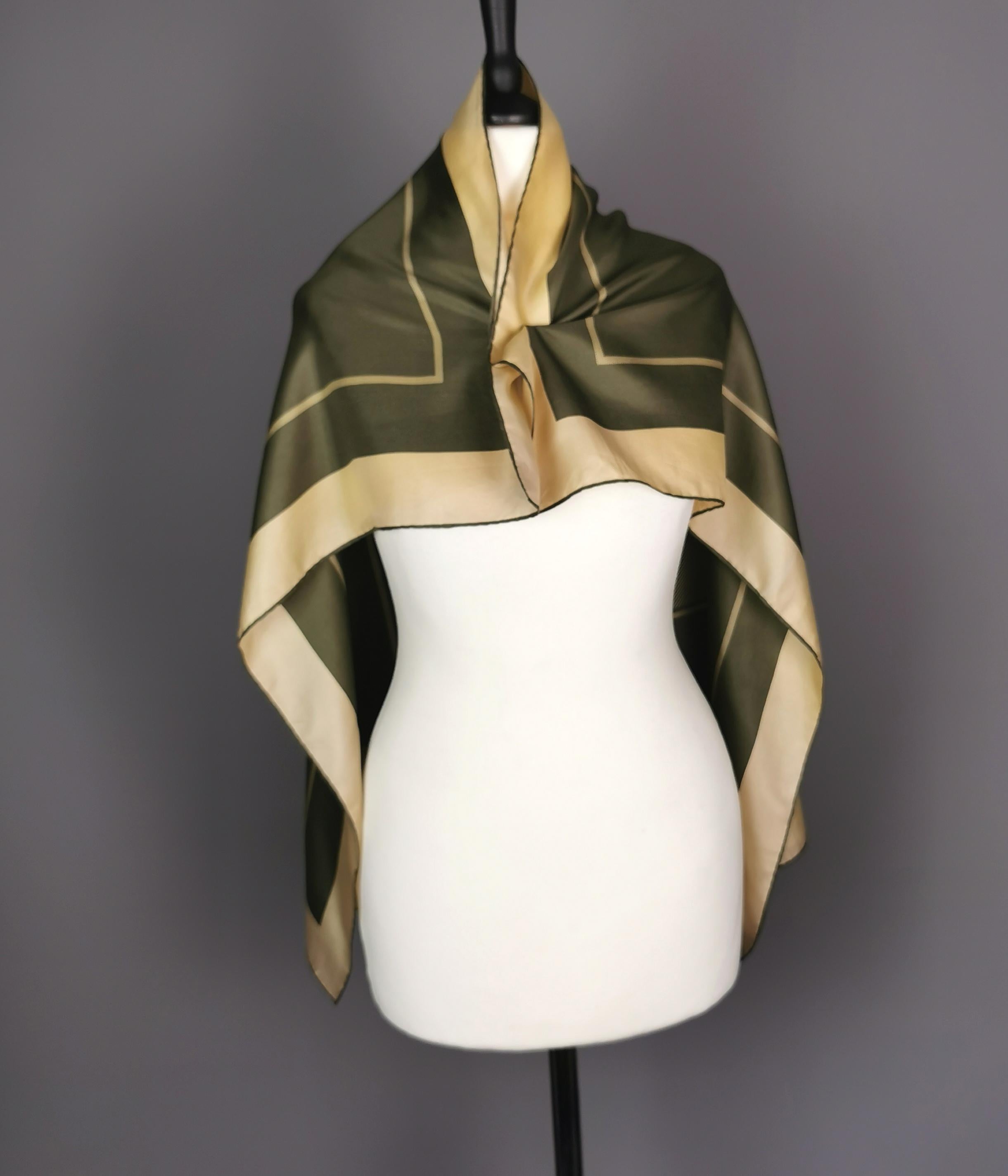 Un magnifique foulard en soie Burberry des années 70.

Fini dans les couleurs vert kaki et beige doré, c'est une écharpe de forme carrée avec une bordure de bloc et une bordure de rayure horizontale et un carré central.

Il est orné du logo Burberry