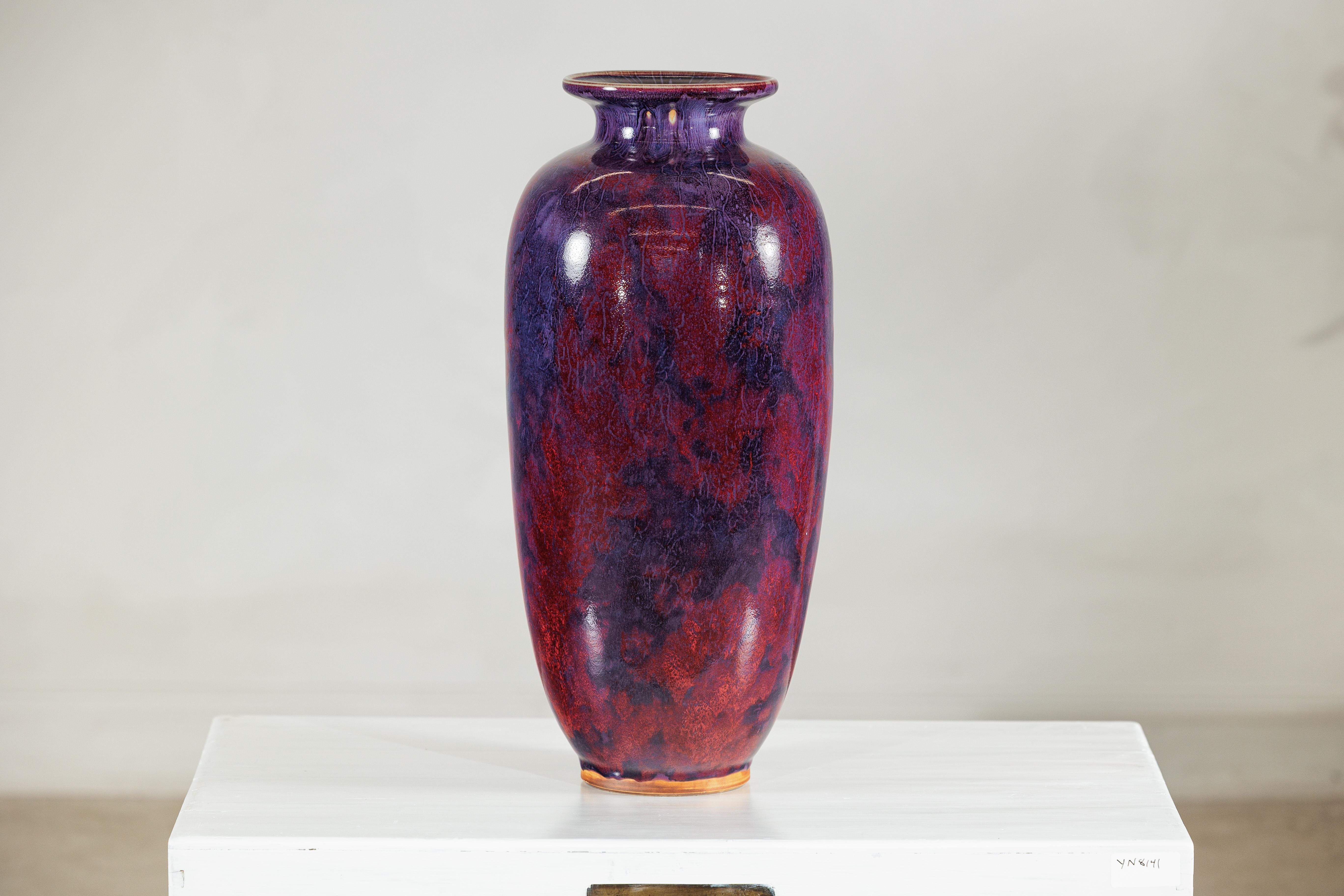 Questo vaso in ceramica vintage cattura l'attenzione con il suo audace gioco di toni profondi di bordeaux, viola e blu, stratificati in uno smalto ricco e fluido. La Silhouette alta e allungata è delicatamente arrotondata con un bordo svasato (con