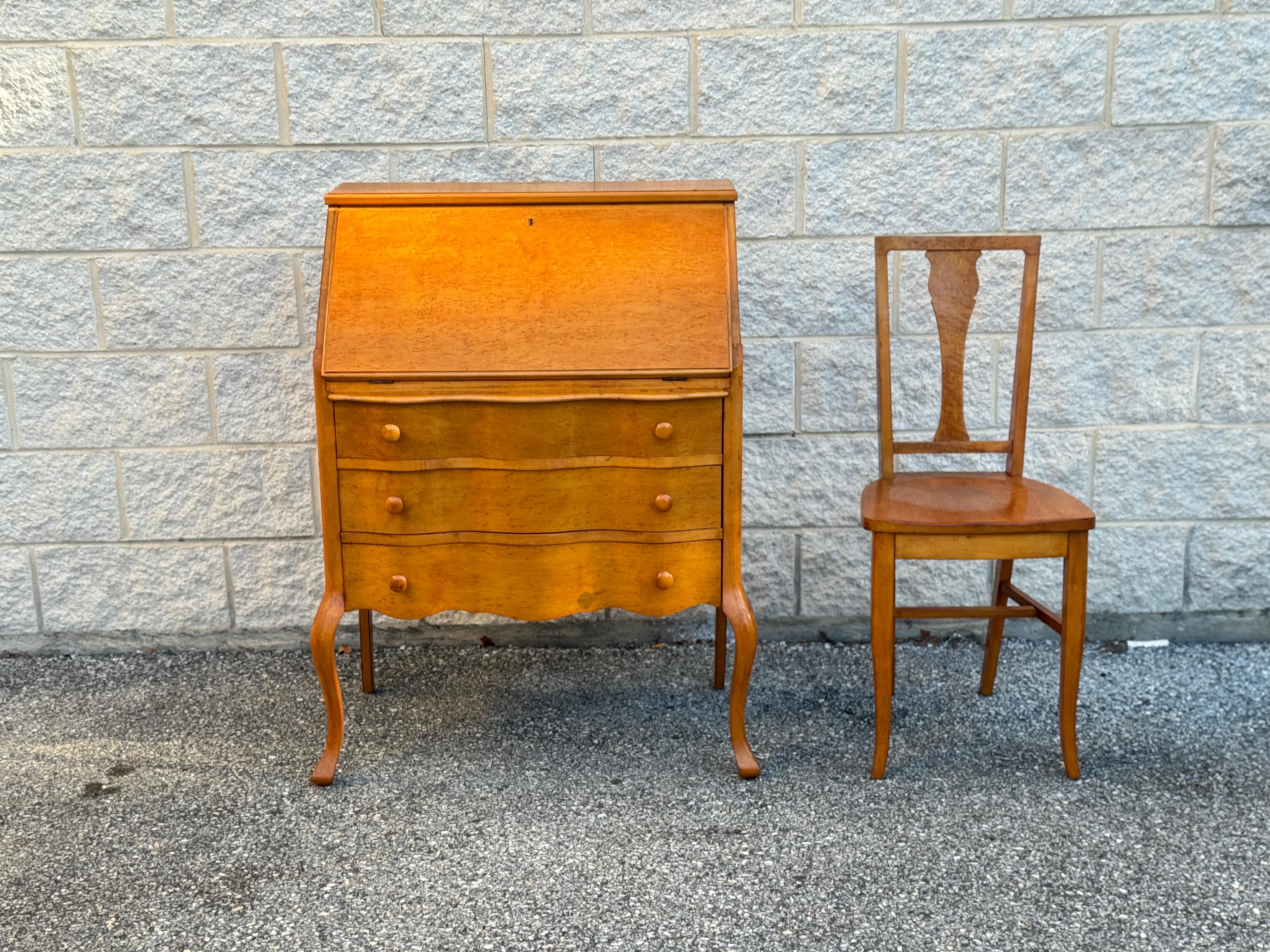 Affascinante scrivania vintage in impiallacciatura di radica con sedia abbinata. La parte anteriore a ribalta si apre per rivelare piccoli scomparti e un cassetto per la cancelleria o i ricordi, mentre la parte inferiore offre cassetti di