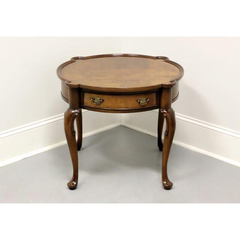 A round accent table in the Queen Anne style, unbranded, similar quality to Baker or Weiman. Burl walnut with brass hardware. Features one dovetail drawer, carved knees, cabriole legs and pad feet. Made in the USA, in the late 20th