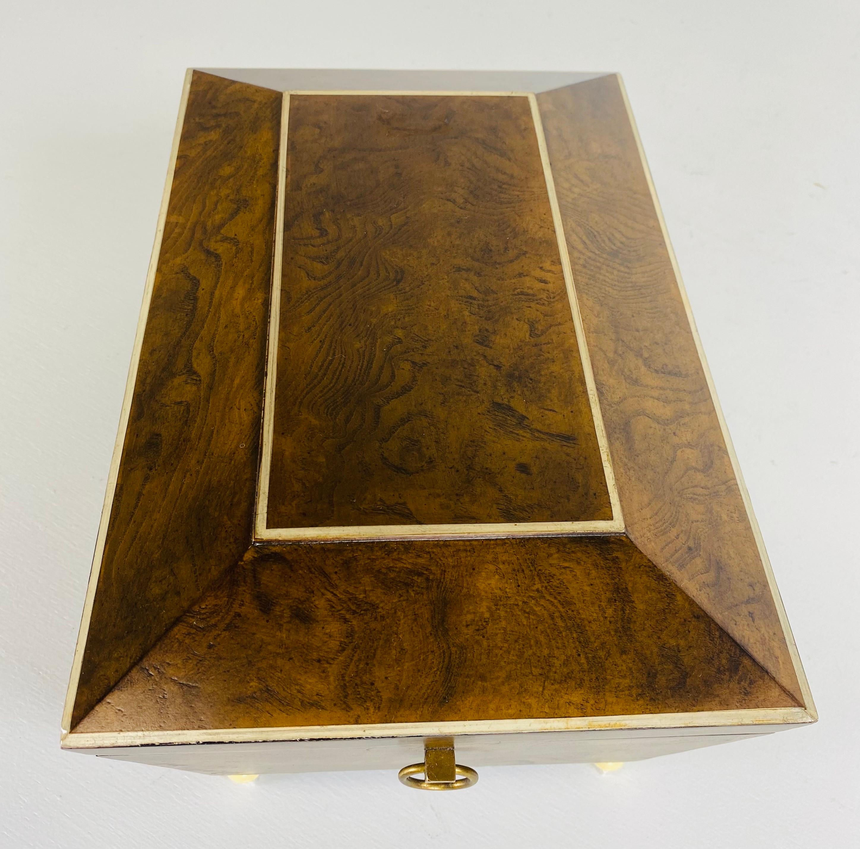 Si tratta di una cassettiera d'epoca in legno di noce burlato alla maniera di Maitland Smith. Questa tavola in noce chiaro è rifinita in finto avorio e ha i piedini a bacchetta in finto avorio. La cassettiera ha due maniglie in ottone su entrambi i