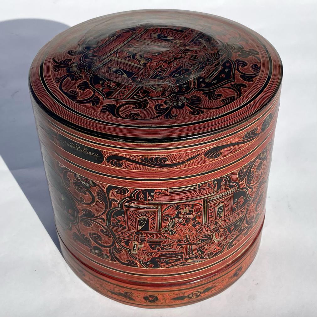 Vintage Burmese Betel Box “Kun-It”, a cylindrical woven container with a deep lid and shallow interior tray, all covered in layers of red black and yellow lacquer having incised decoration in reserves depicting kings and palaces 
Minor cracks and