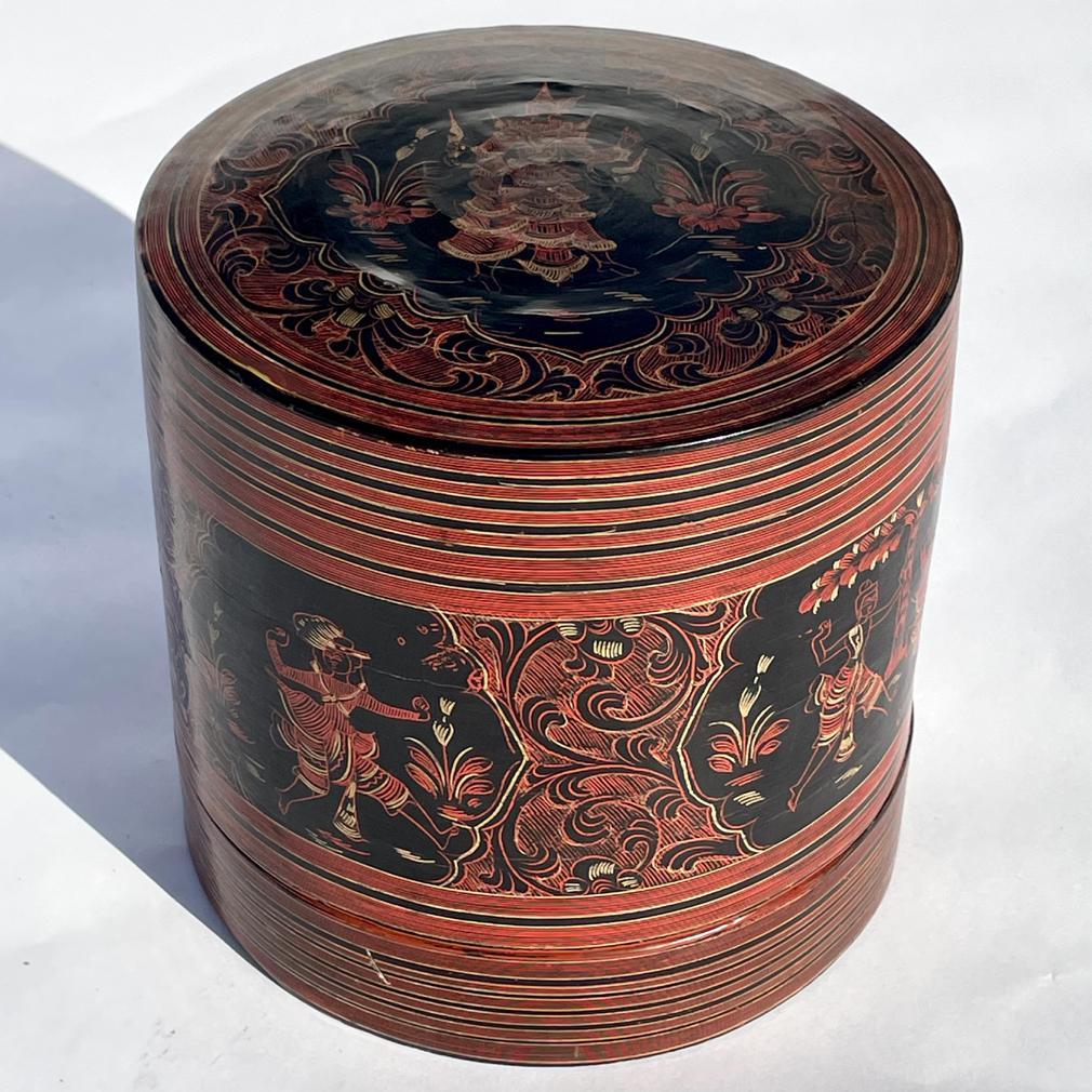 Vintage Burmese Betel Box “Kun-It”, a cylindrical woven container with a deep lid and shallow interior tray, all covered in layers of red black and yellow lacquer having incised decoration in reserves depicting dancers within scrolling foliate vine