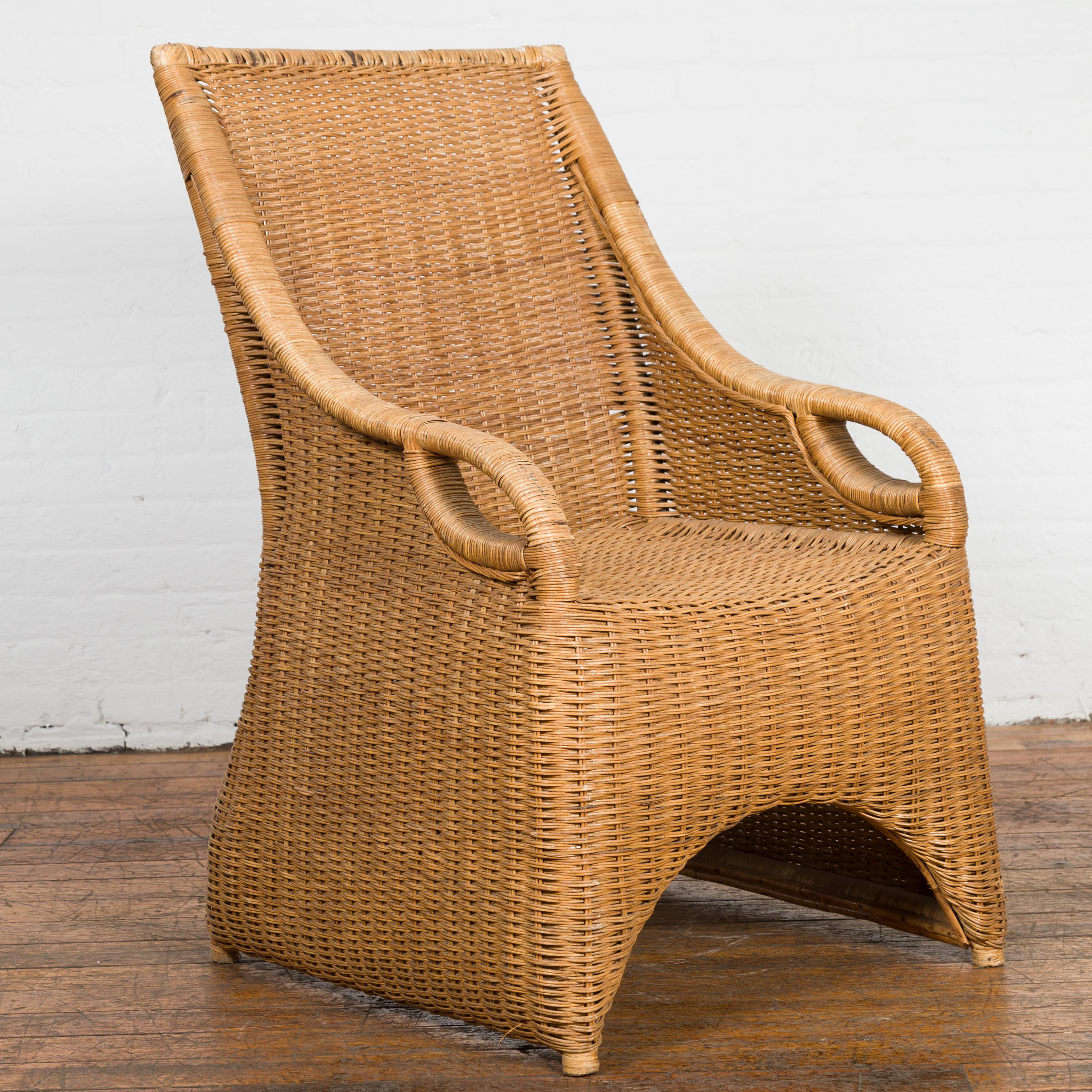 A vintage Burmese Country style woven rattan lounge chair from the Mid-20th Century, with slanted rectangular back, curving arms, looping accents and arching base. Created in Burma during the midcentury period, this Country style lounge chair