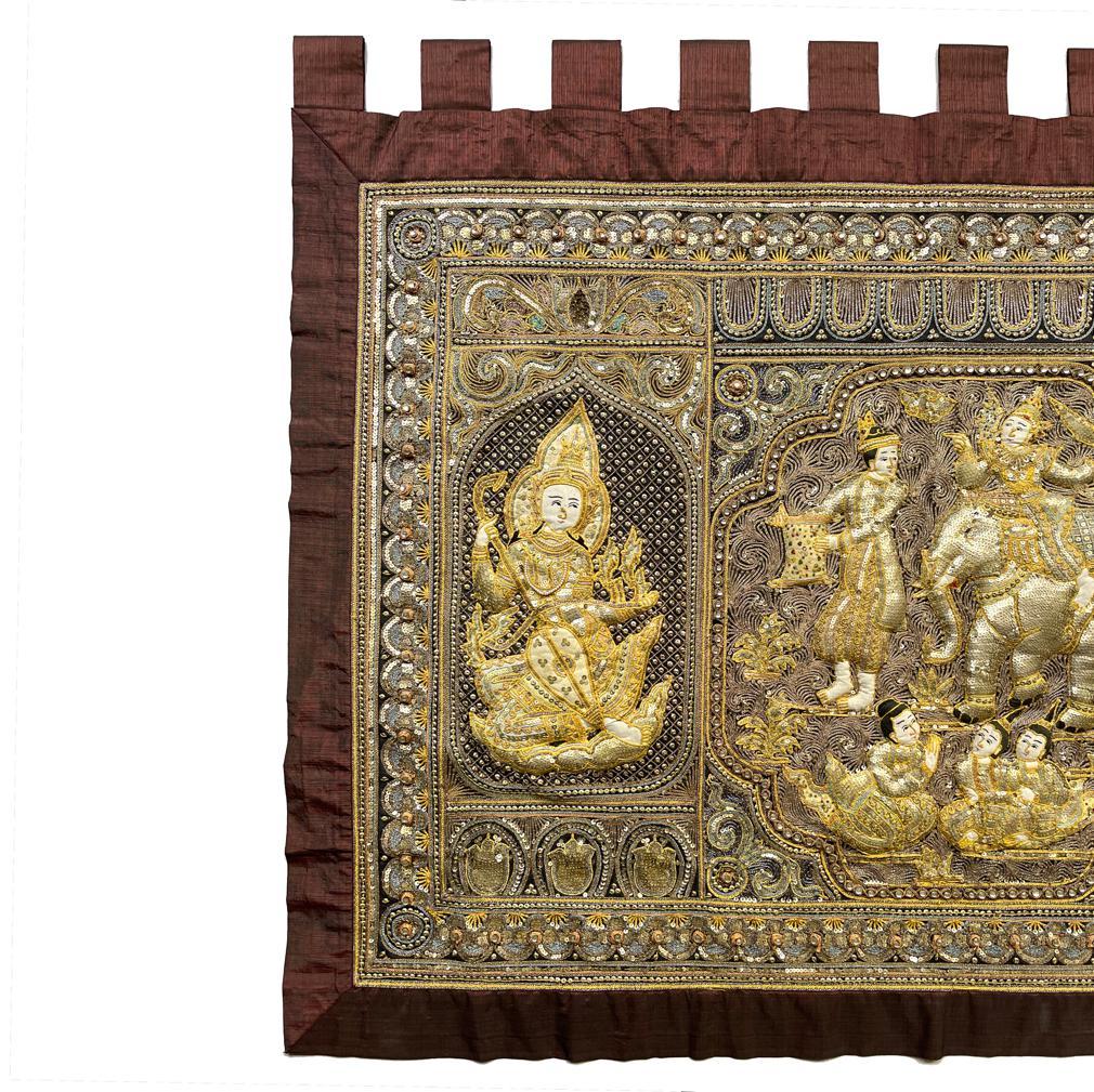 Vintage Burmese Kalaga, Mandalay.
A wall hanging embroidered tapestry inspired from a scene in the Jataka Tales. The embroidery depicts a prince riding a white elephant led by an attendant holding a muti-colored feed bag with three devotional
