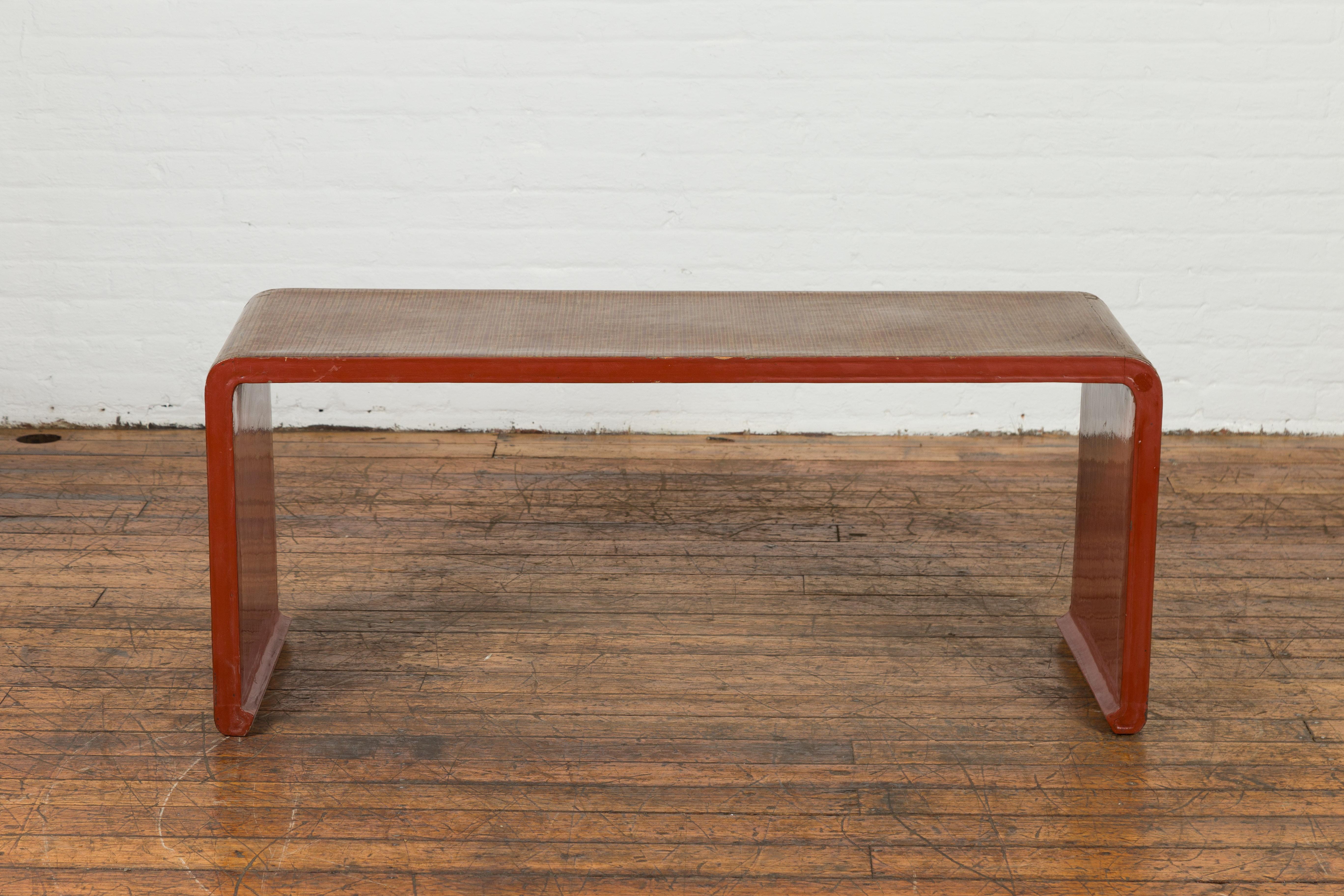 A vintage Burmese red lacquered waterfall coffee table from the Mid-20th century with Negora lacquered top, Japanese inspired design and scrolling extremities. Created in Burma during the Midcentury period, this waterfall coffee table features a