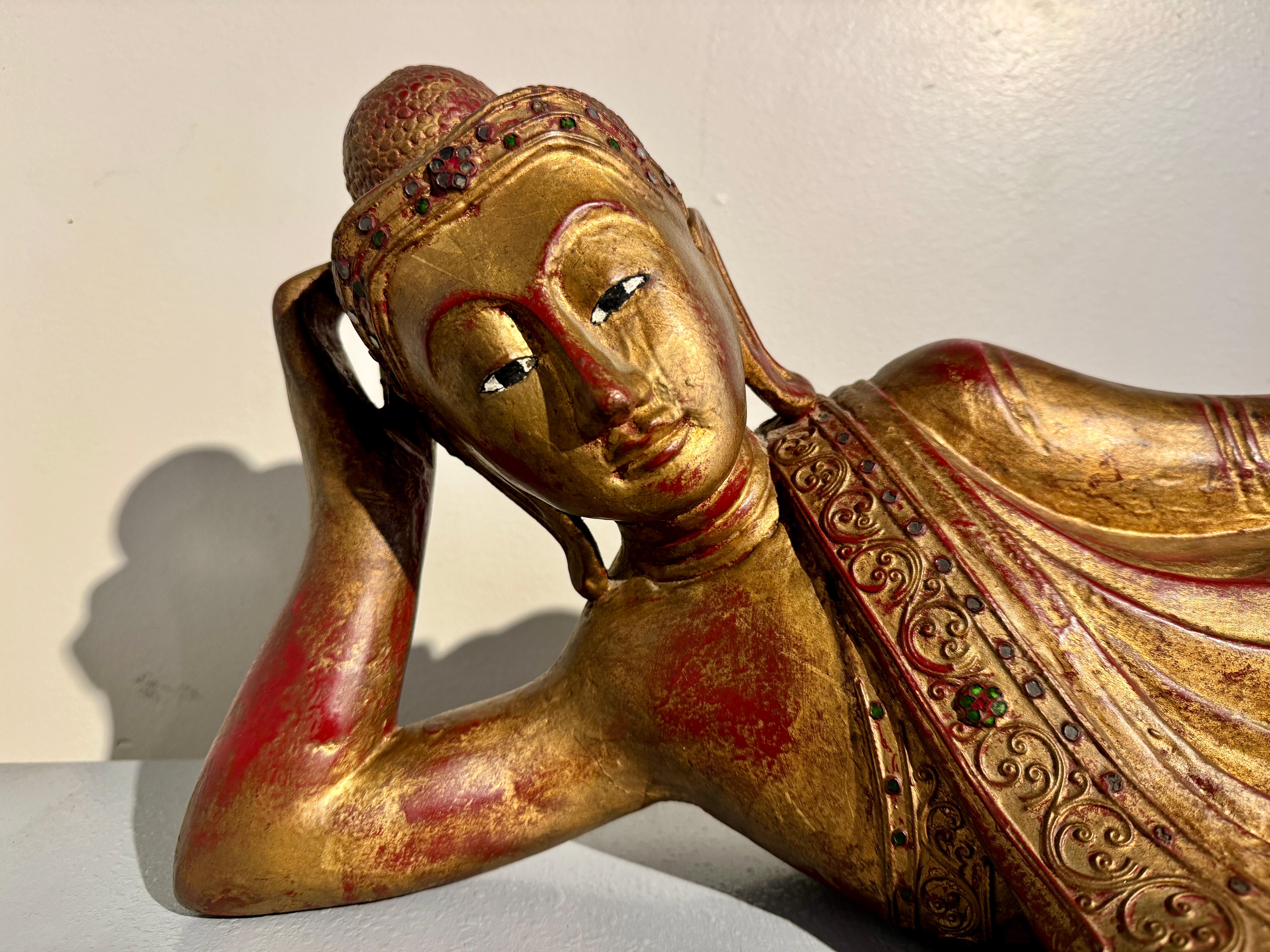 A charming vintage Burmese Mandalay Style carved, lacquered, and gilt wood figure of a reclining Buddha, 1970's, Burma.

The delightful Buddha figure is portrayed resting comfortably and elegantly on his side, supporting his weight on one elbow, his