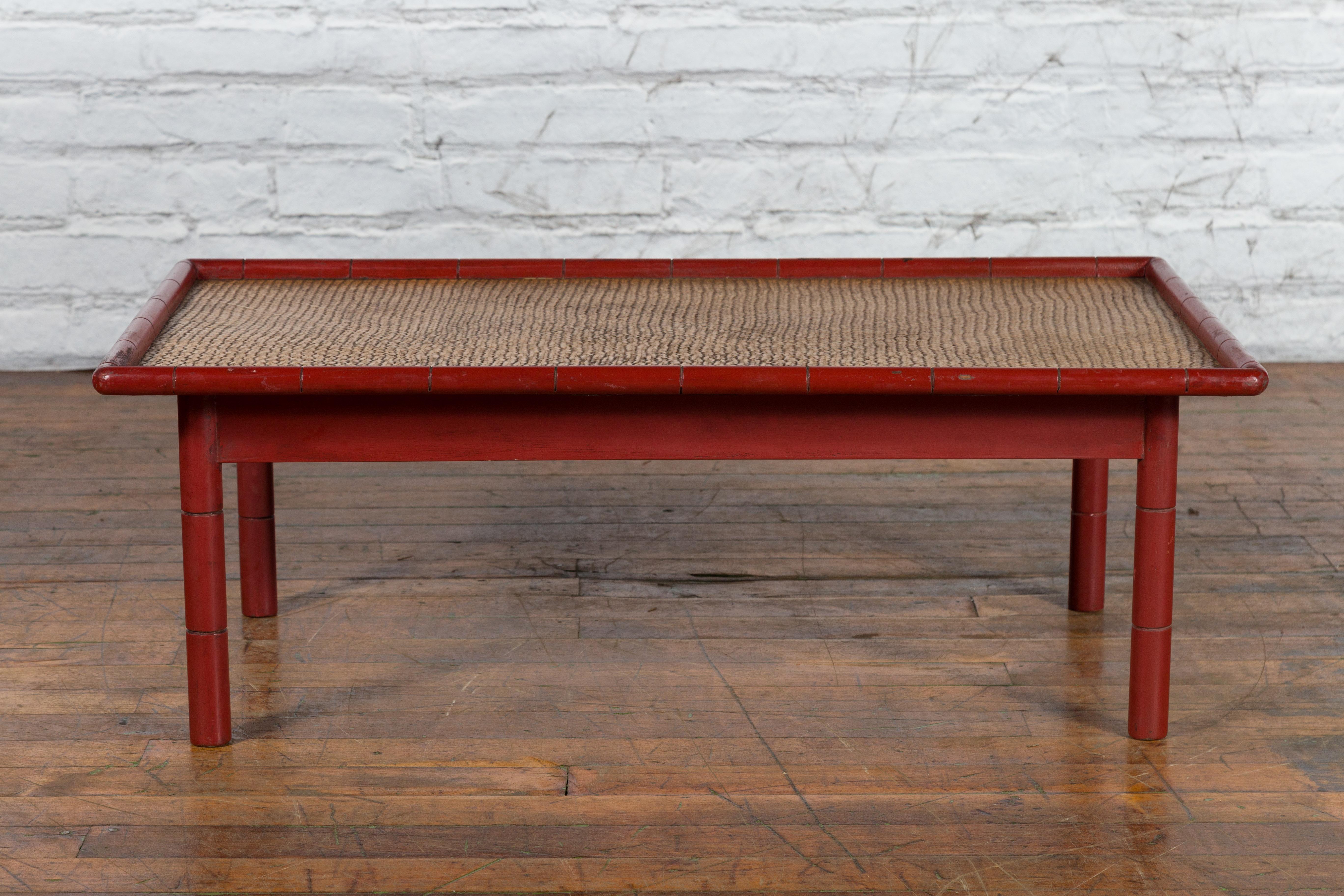 A vintage Country style Burmese red lacquered faux bamboo coffee table from the mid 20th century with woven rattan top and straight legs. Created in Burma during the Midcentury period, this rustic coffee table features a rectangular woven rattan top