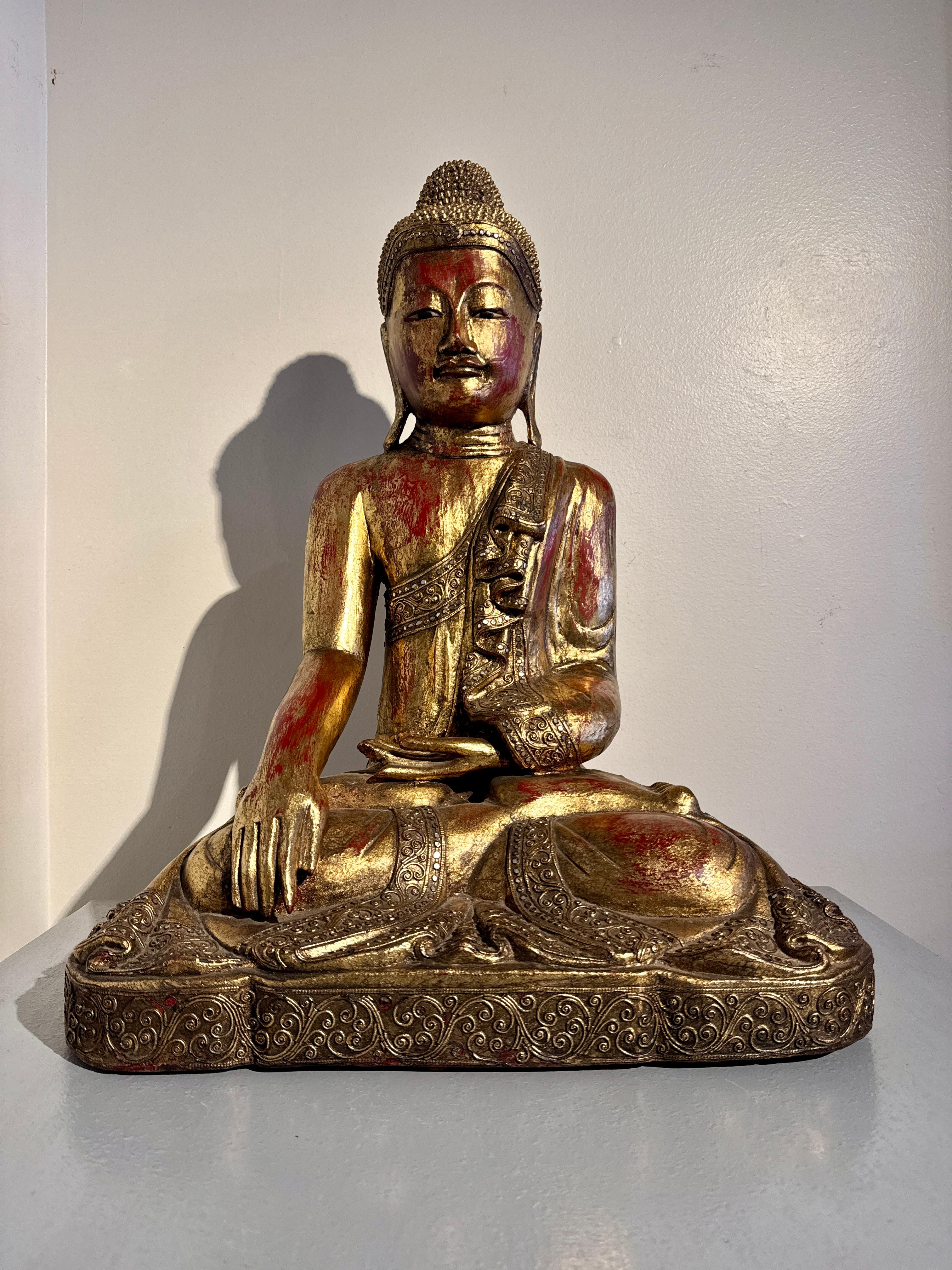 A large and serene vintage sculpture of the historical Buddha, Shakyamuni, carved of teak wood, gilt, and embellished with glass 