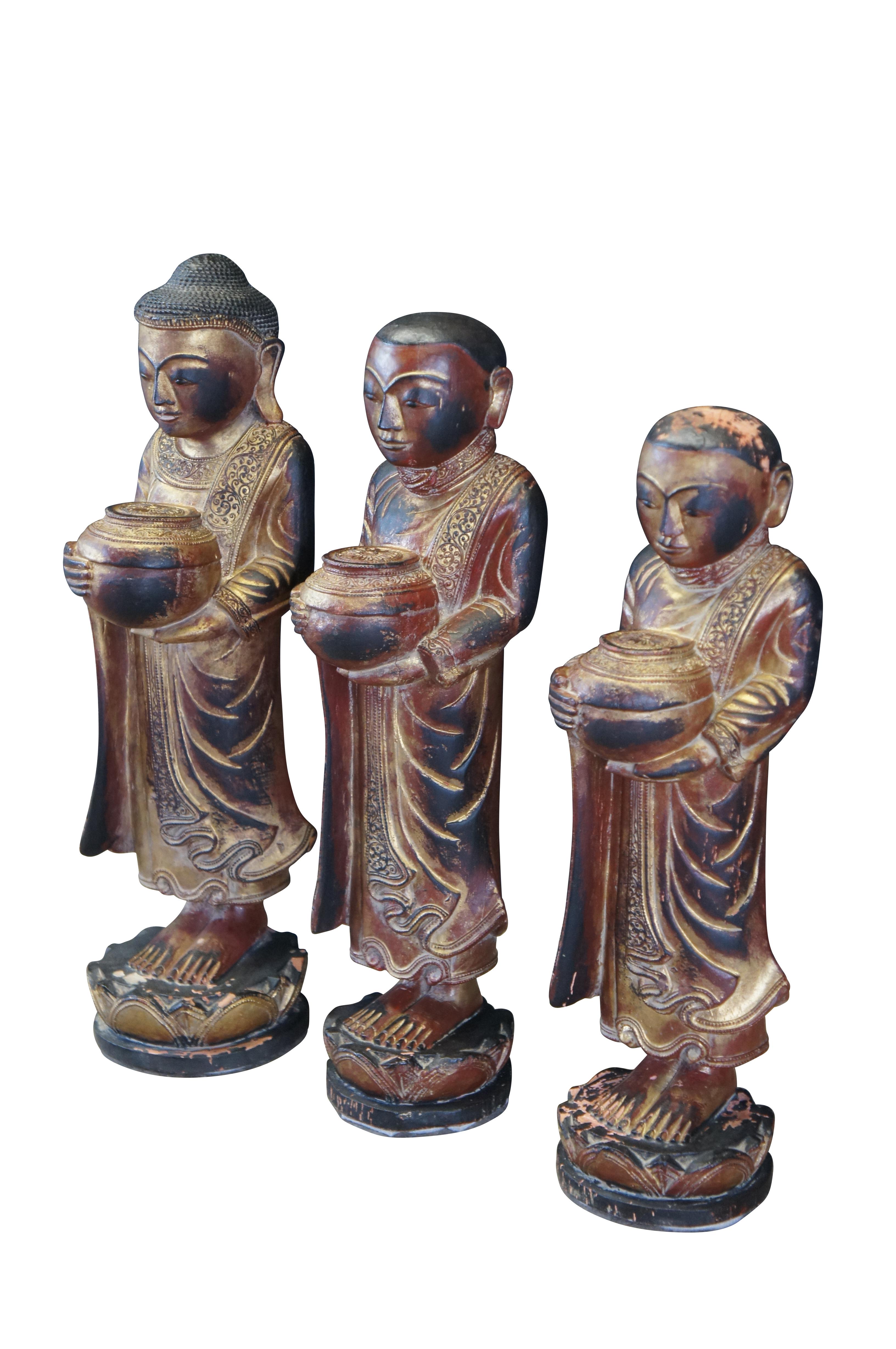Three vintage carved Burmese / Thai buddha / monk statues.  Carved of wood featuring figures dressed in traditional attire holding bowls or prayer offerings and standing on lotus flowers.

Dimensions:
7