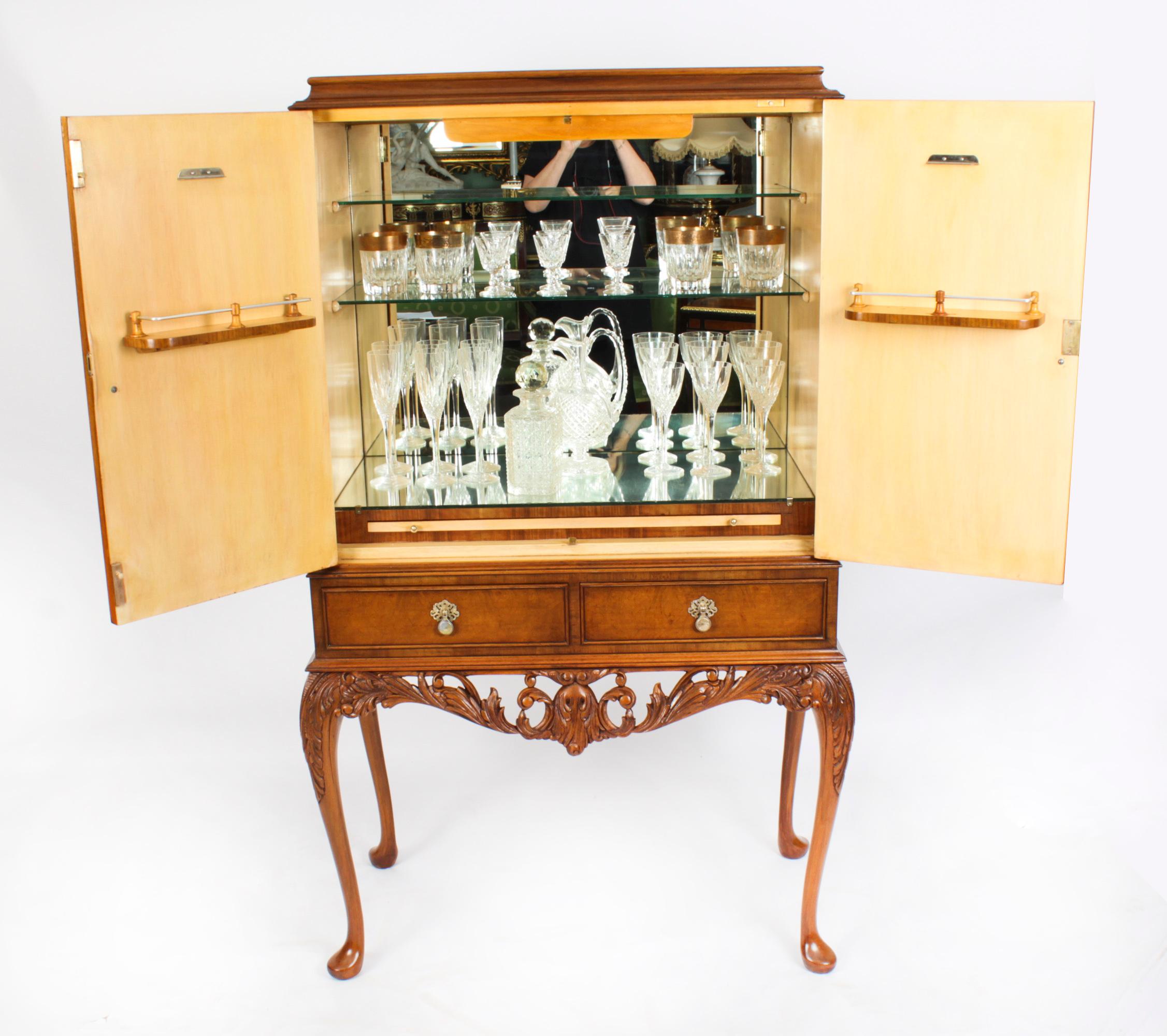 Mid century burr walnut cocktail drinks cabinet, two doors, glass shelves with mirrored back base and brush slide, above two drawers, raised on carved cabriole legs. Measures: height 60