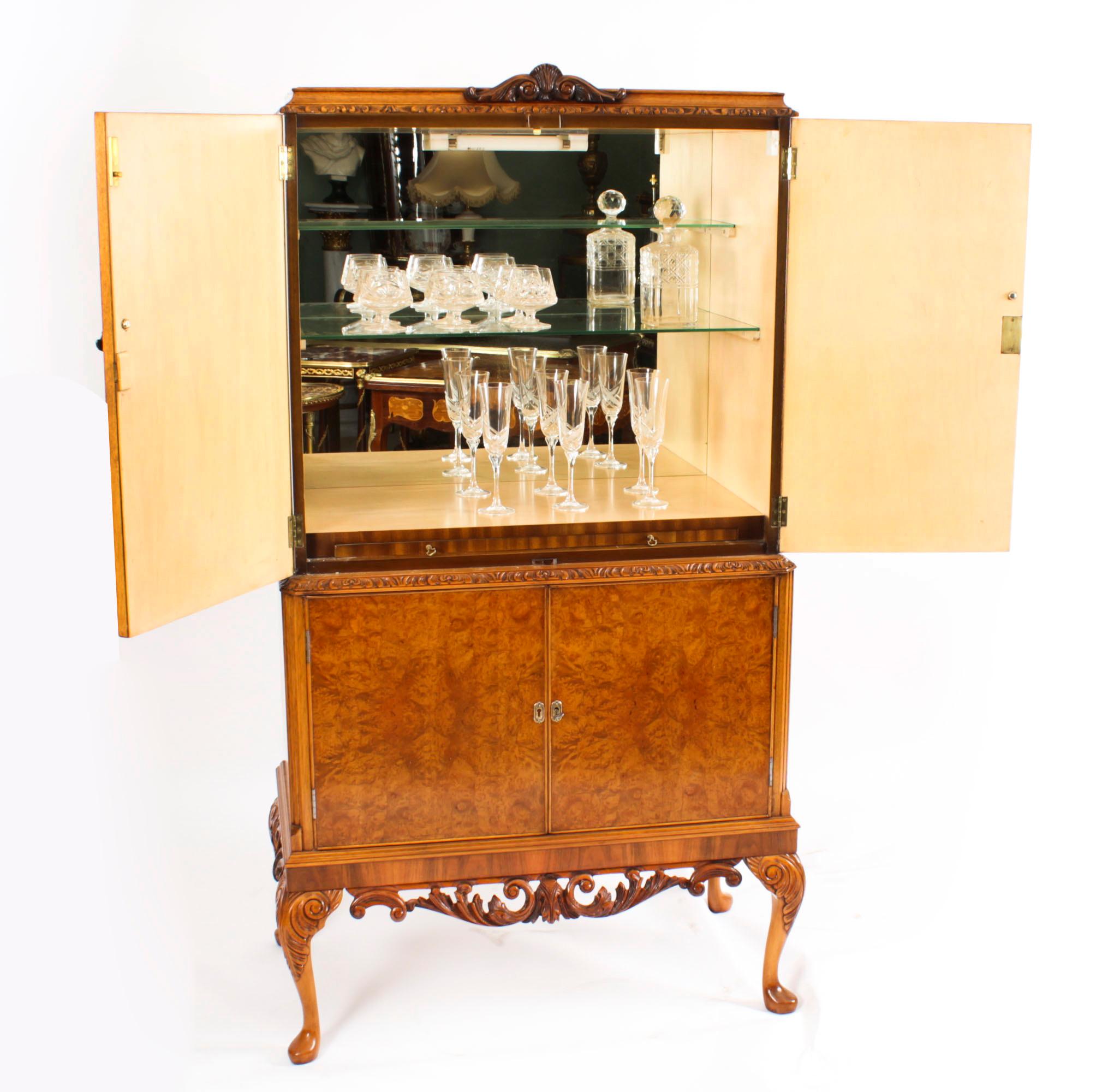 This is a fantastic vintage burr walnut cocktail cabinet with fitted and mirrored maple interior, dating from the Mid-20th Century.
 
The upper part comprises a carved crest above a pair of doors with decorative hinges and a large central