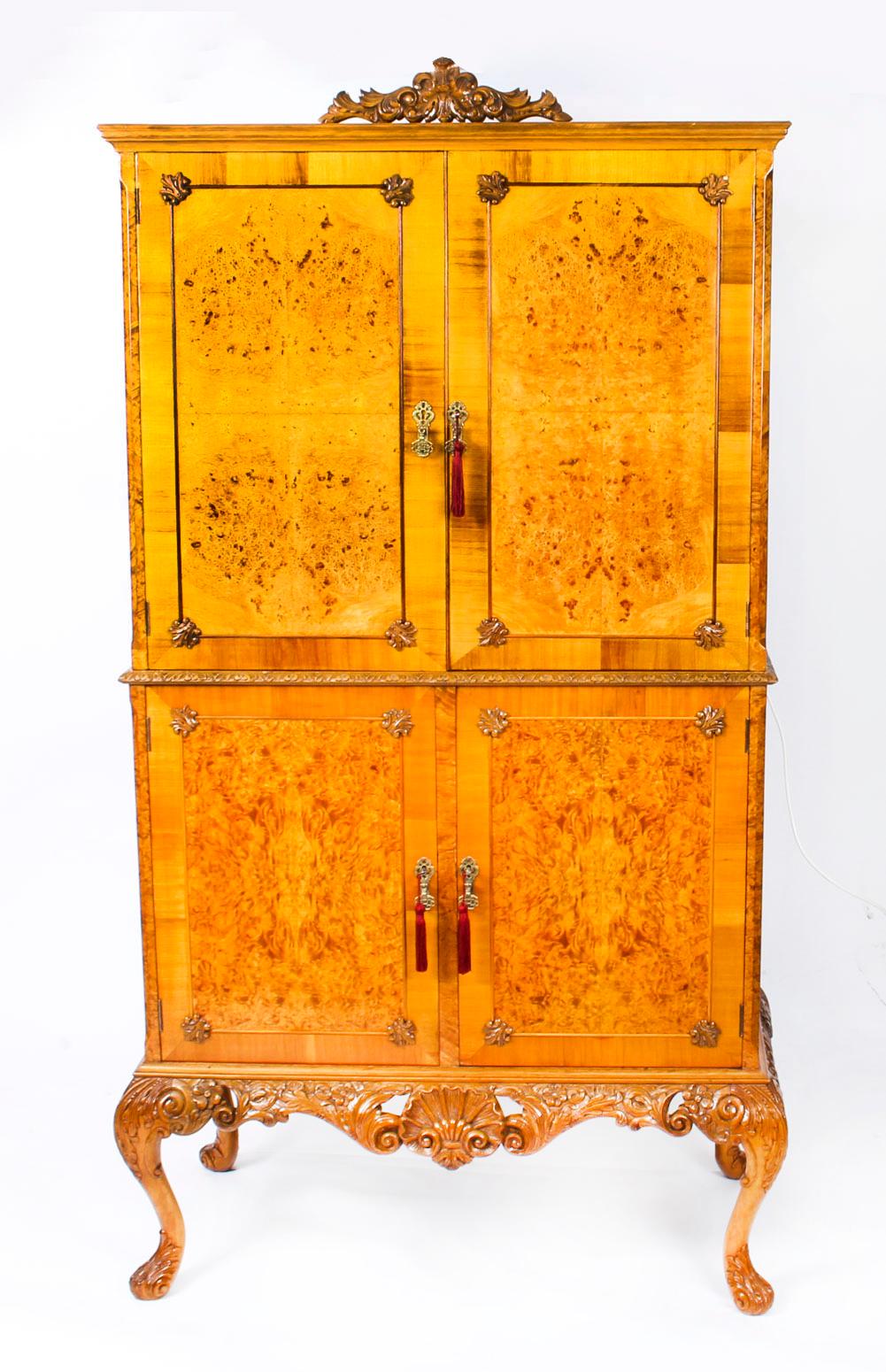 This is a fantastic vintage burr walnut cocktail cabinet in Queen Anne style, dating from the mid-20th century.
 
The beautifully figured burr walnut two-tier cocktail cabinet features a scroll carved crest to the top, the pair of panelled doors