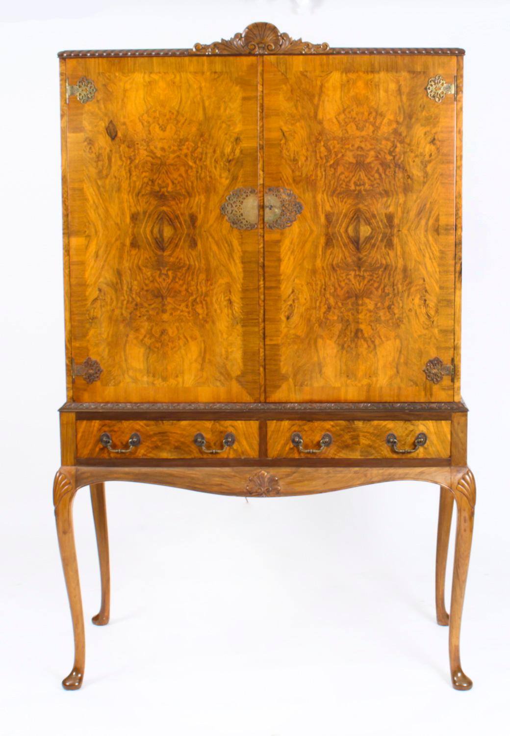 This is a fantastic vintage Queen Anne Revival burr walnut cocktail cabinet with wonderful hand carved decoration dating from the early 20th Century.
 
The cabinet features a carved cresting, the doors open to reveal a stunning fitted mirrored