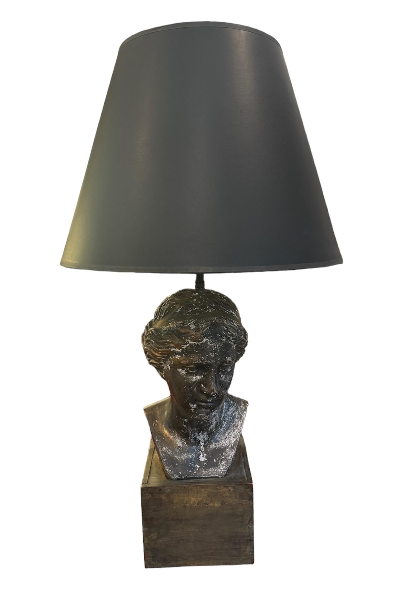 Illuminate your space with distinctive flair using this unique table lamp featuring a female bust as its base atop a cube wood plinth. The lamp exudes artistic charm with its bronze-toned finish on the base, while adding a touch of vintage elegance.