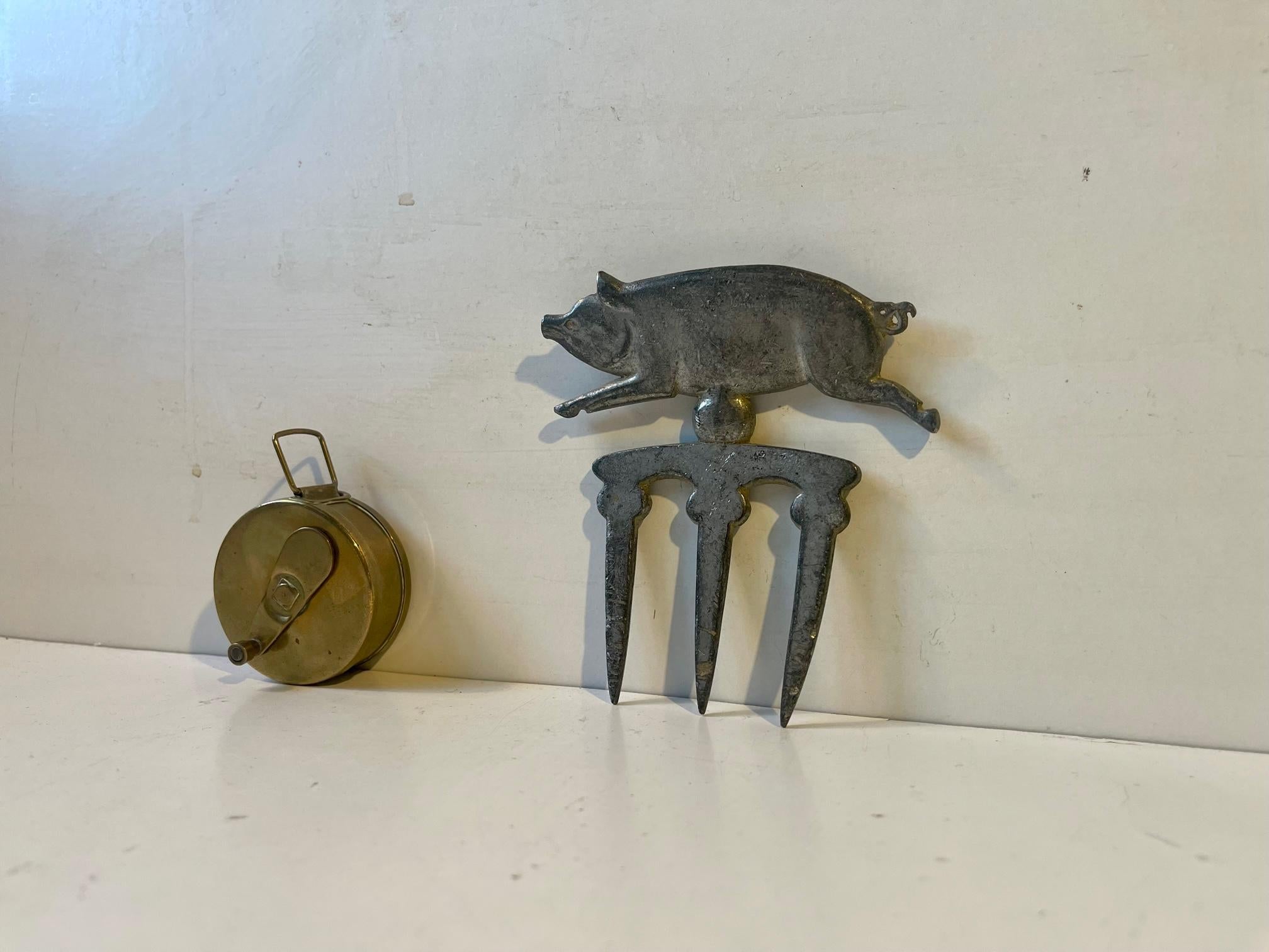 Unusual set of butcher accessories. A solid brass measuring tape dispenser for measuring the chest/feed level (text in Danish) of livestock both pigs and cows and a 1930s pork meat display stick-in sign in zink or pewter. Measurements: dispenser: 5