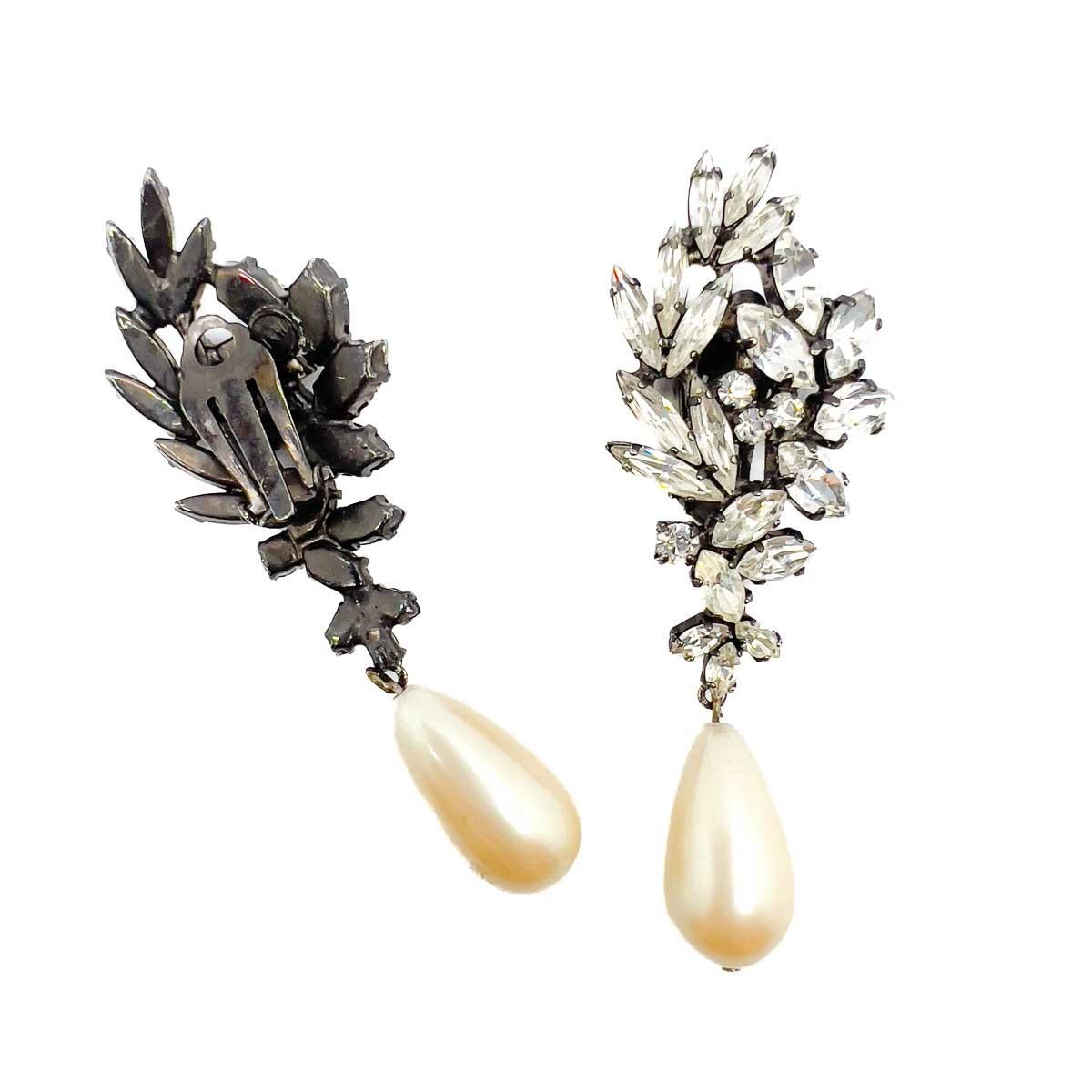 A pair of Vintage Butler & Wilson Crystal & Pearl Droplet Earrings. Exquisite navette cut stones in a stone rich setting are finished to perfection with a large drop pearl. The epitome of elegance.


Butler and Wilson began in 1969 selling antique