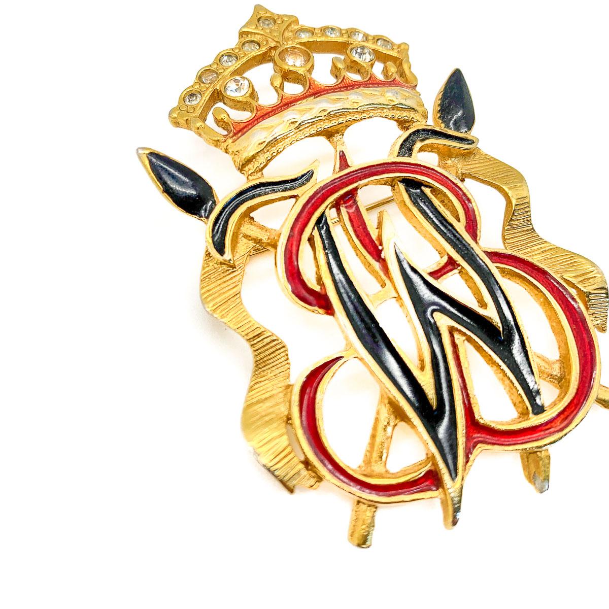Eine heraldische Brosche von Butler & Wilson aus den 1980er Jahren. Er ist aus vergoldetem Metall gefertigt und mit Emaille und Strasssteinen verziert, die die ineinander verschlungenen Initialen des weltberühmten Schmuckunternehmens zieren. In sehr