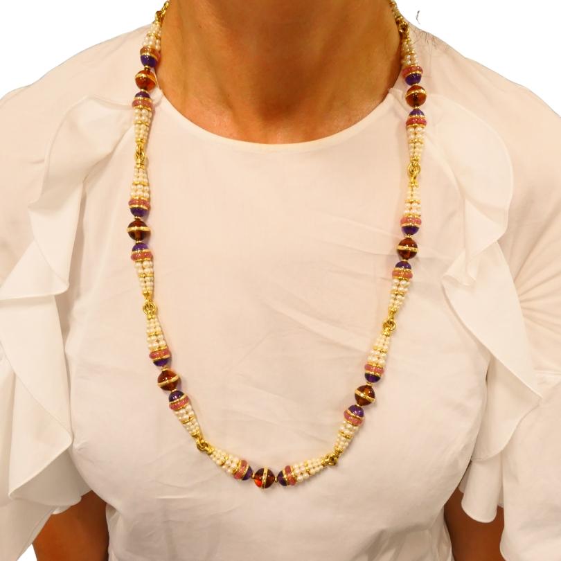 A striking vintage Bulgari necklace, made of 18k gold, featuring gemstones and pearls.
The necklace consists of tapered clusters of pearls alternating with spherical gemstone beads that are separated by the gold rings.  The gemstones are pink