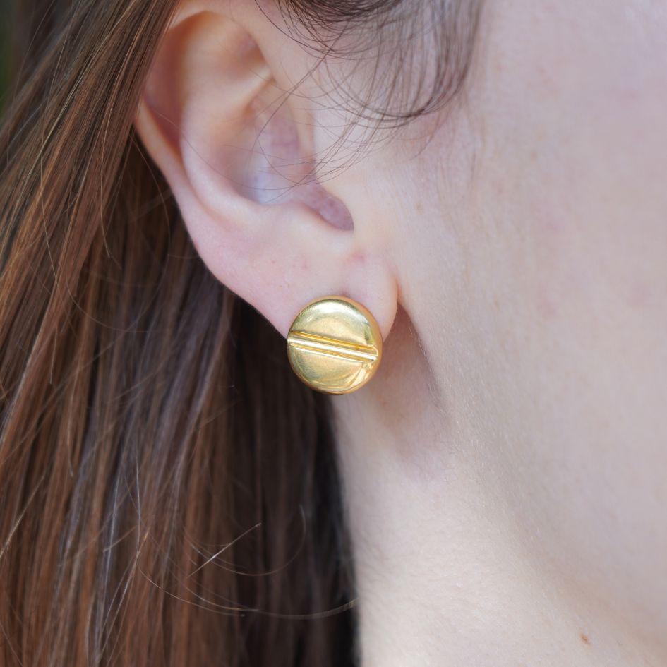 These vintage Bvlgari button earrings are crafted in 20 karat yellow gold with 18k yellow gold clasps. Designed as a domed circular stud with a recessed groove across the center, they reflect the minimalist and bold styling often seen in Bvlgari’s