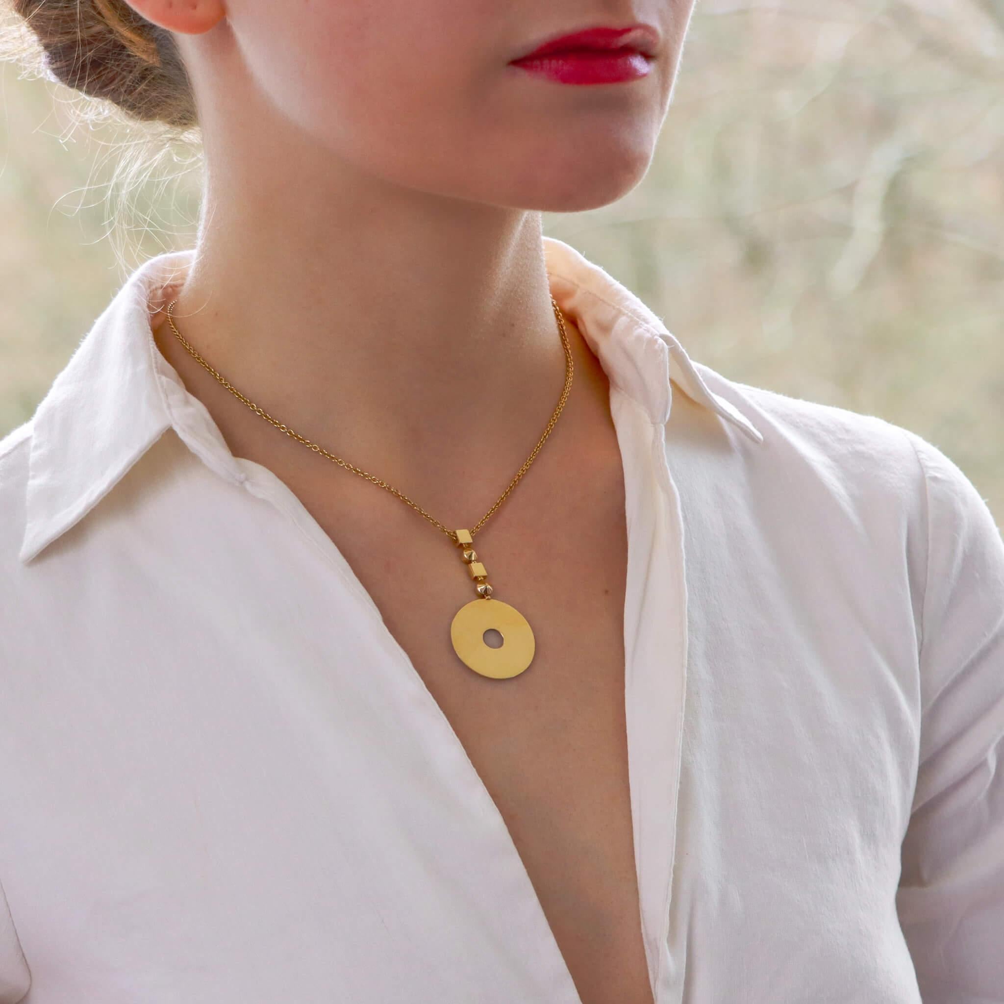 A beautiful vintage Bvlgari circular disc pendant set in solid 18k yellow gold.

The pendant is composed of a solid 18k polished yellow gold disc pierced centrally with a circular opening. The disc suspends from a geometric inspired bail composed of