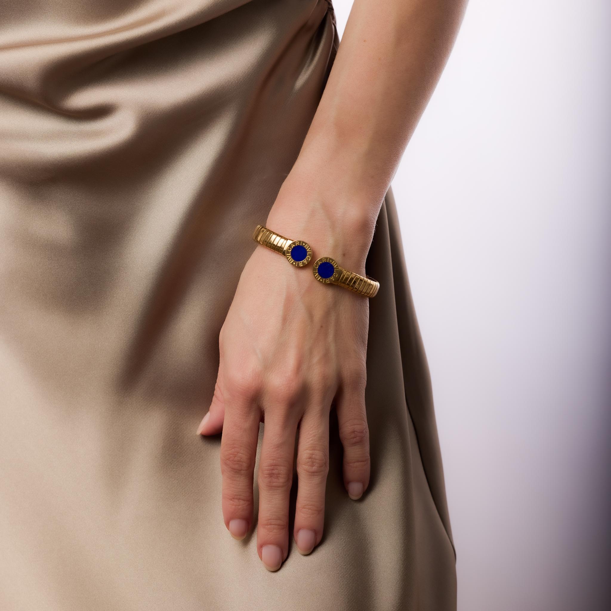 This vintage Bvlgari Tubogas cuff bracelet in 18k yellow gold features two round cut lapis lazuli stones, approximately 7.84mm each. A striking blend of bold design and timeless craftsmanship, this iconic piece is signed Bvlgari and hallmarked with