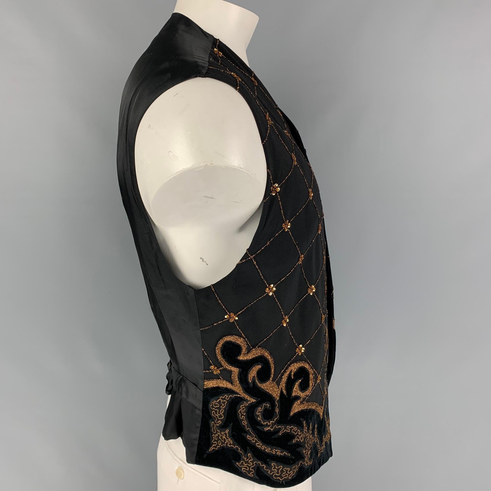 Vintage BYBLOS vest comes in a black wool featuring gold embroidered designs, velvet trim, back belt strap, and a buttoned closure. Made in Italy. 

Very Good Pre-Owned Condition.
Marked: 52

Measurements:

Shoulder: 19.5 in.
Chest: 42 in.
Length: