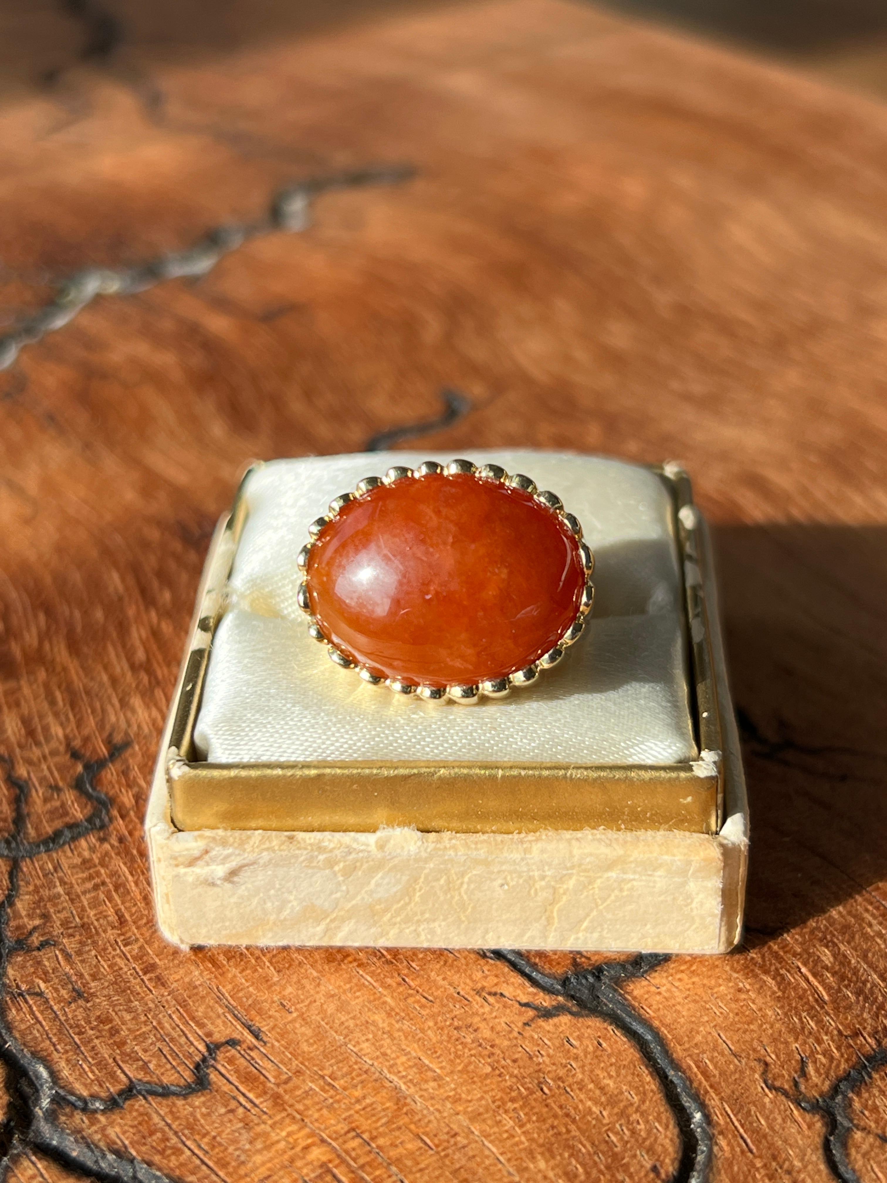 This vintage 18K yellow gold cocktail ring highlights a striking east-to-west bezel-set cabochon carnelian, measuring 18.07mm x 14.06mm. The rich warmth of the carnelian is complemented by the ring’s fluted shank, which tapers from 11.85mm to