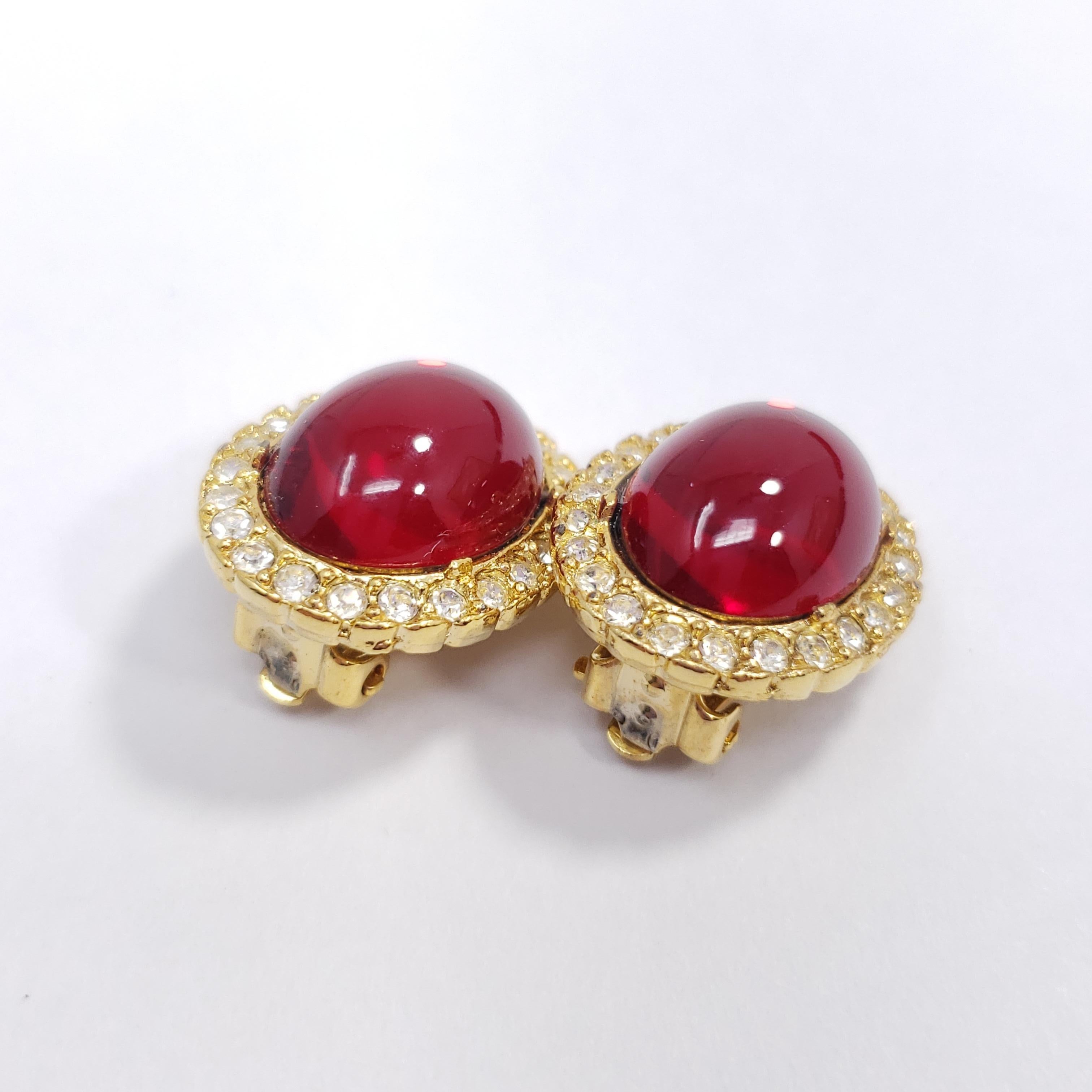 A pair of  exquisite clip on earrings, each featuring a single, royal, ruby-red cabochon accented with smaller crystals, set on a golden clip.

Gold-filled. Made in the USA. Circa mid to late 20th century.

Each earring approx. 1 inch by 0.7 inch