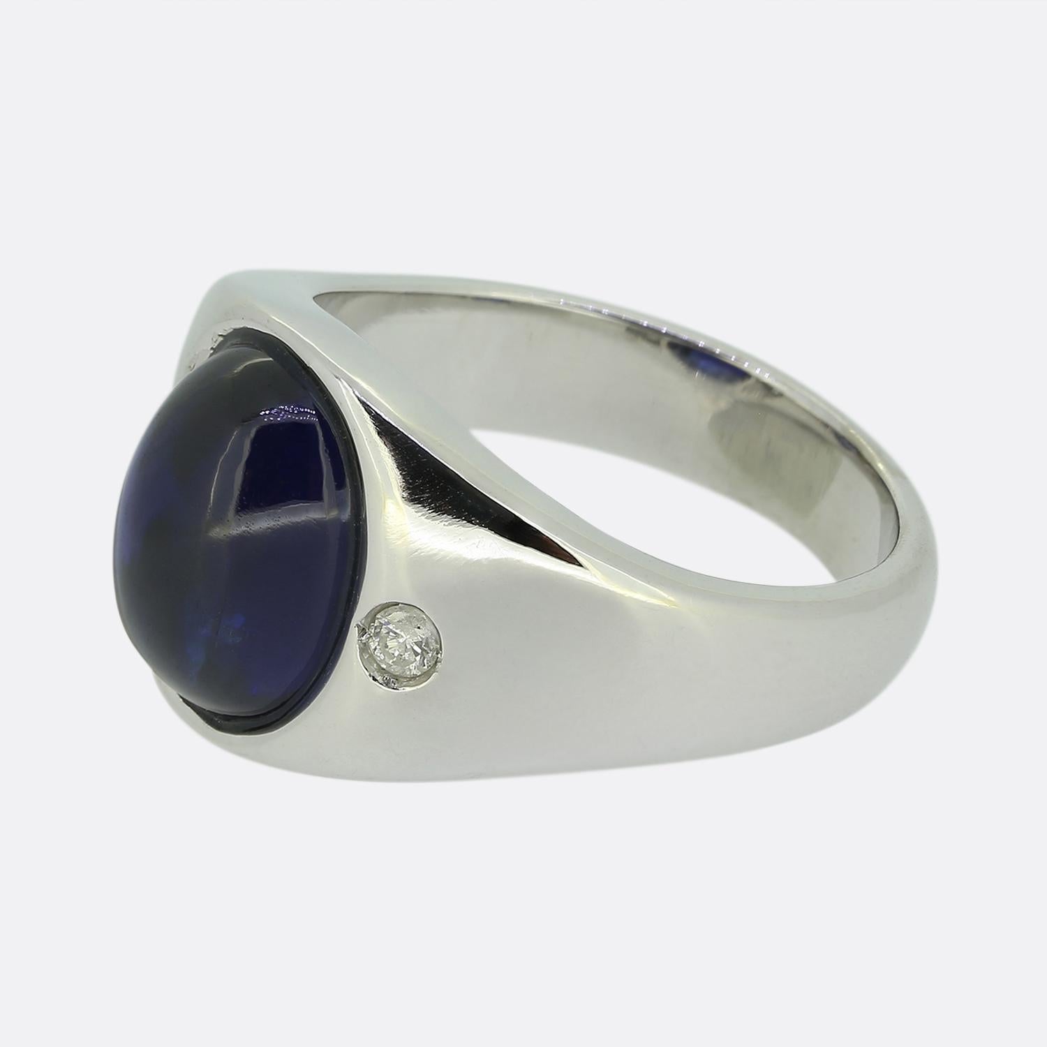 Ecco un anello a tre pietre elegante e raffinato. Al centro del quadrante si trova uno zaffiro cabochon liscio di colore blu scuro. Questa pietra focale è affiancata ai lati da un singolo diamante bianco rotondo taglio brillante. L'anello è